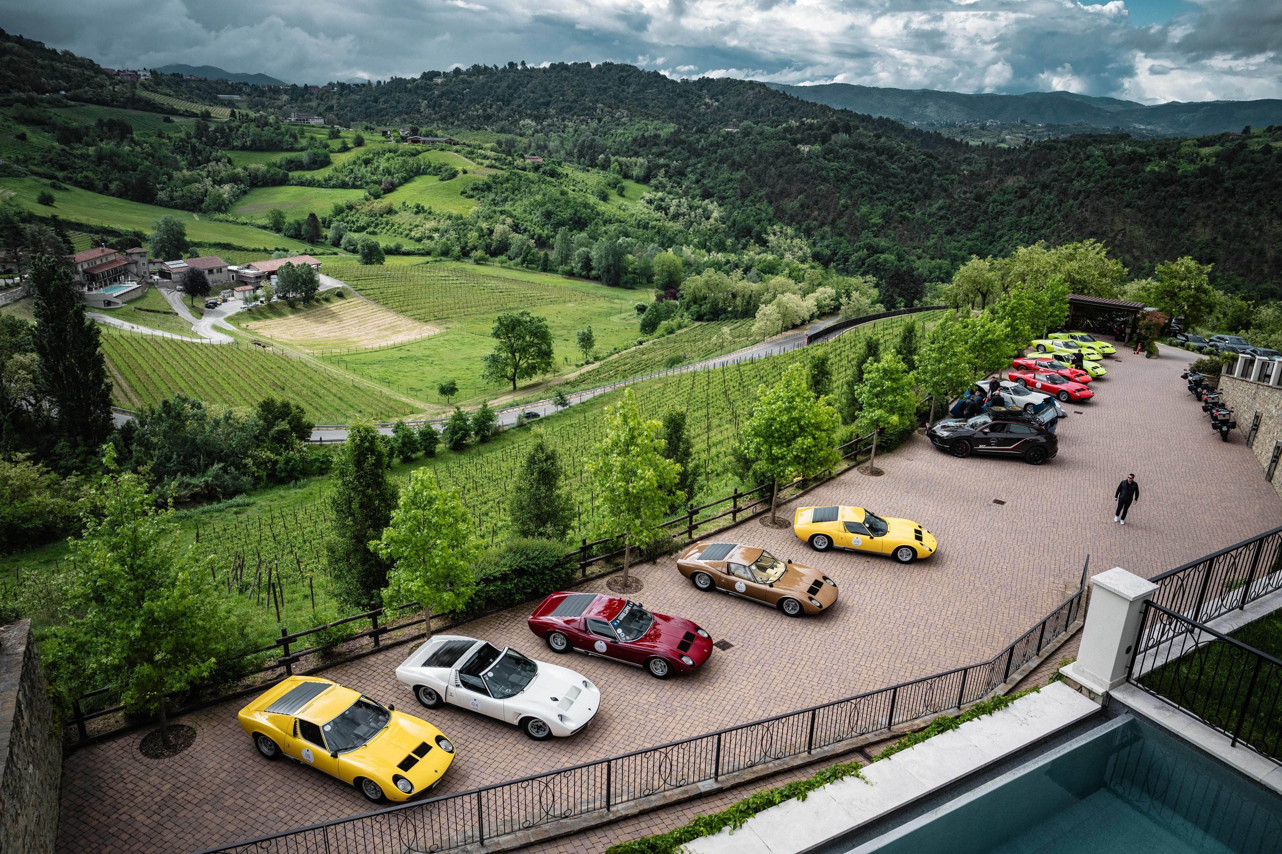 Twenty Miuras, 500 Kilometers, And One Fenomeno Roadster: Inside Lamborghini'S 2026 Polo Storico Giro 9 Panoramic view of lamborghini miuras parked on a brick terrace overlooking a vast green valley with vineyards and hills under dramatic clouds