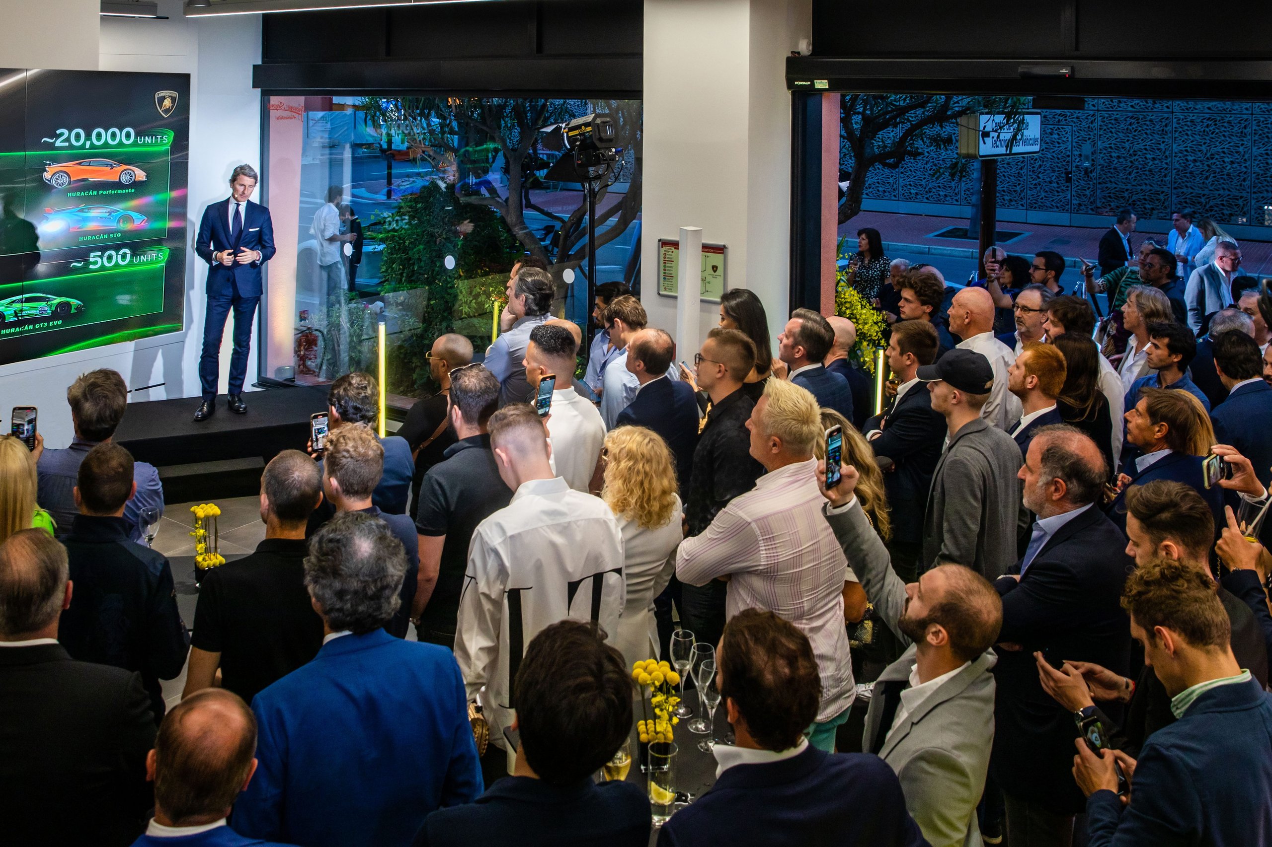 Lamborghini Monaco: How A 218-Square-Meter Showroom Became The Brand'S Riviera Calling Card 13 Executive presenting on stage with lamborghini models displayed on a large screen to an audience at the monaco dealership opening