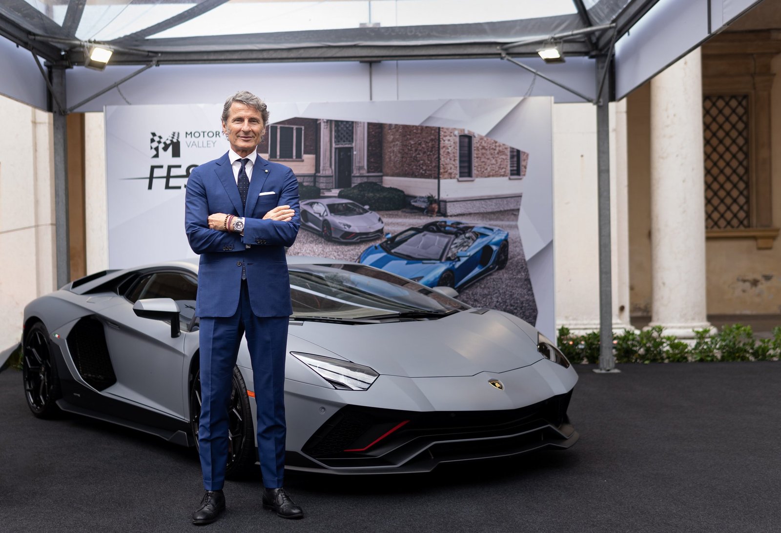 A Lamborghini executive stands beside a grey Aventador Ultimae at Motor Valley Fest 2022 in Modena