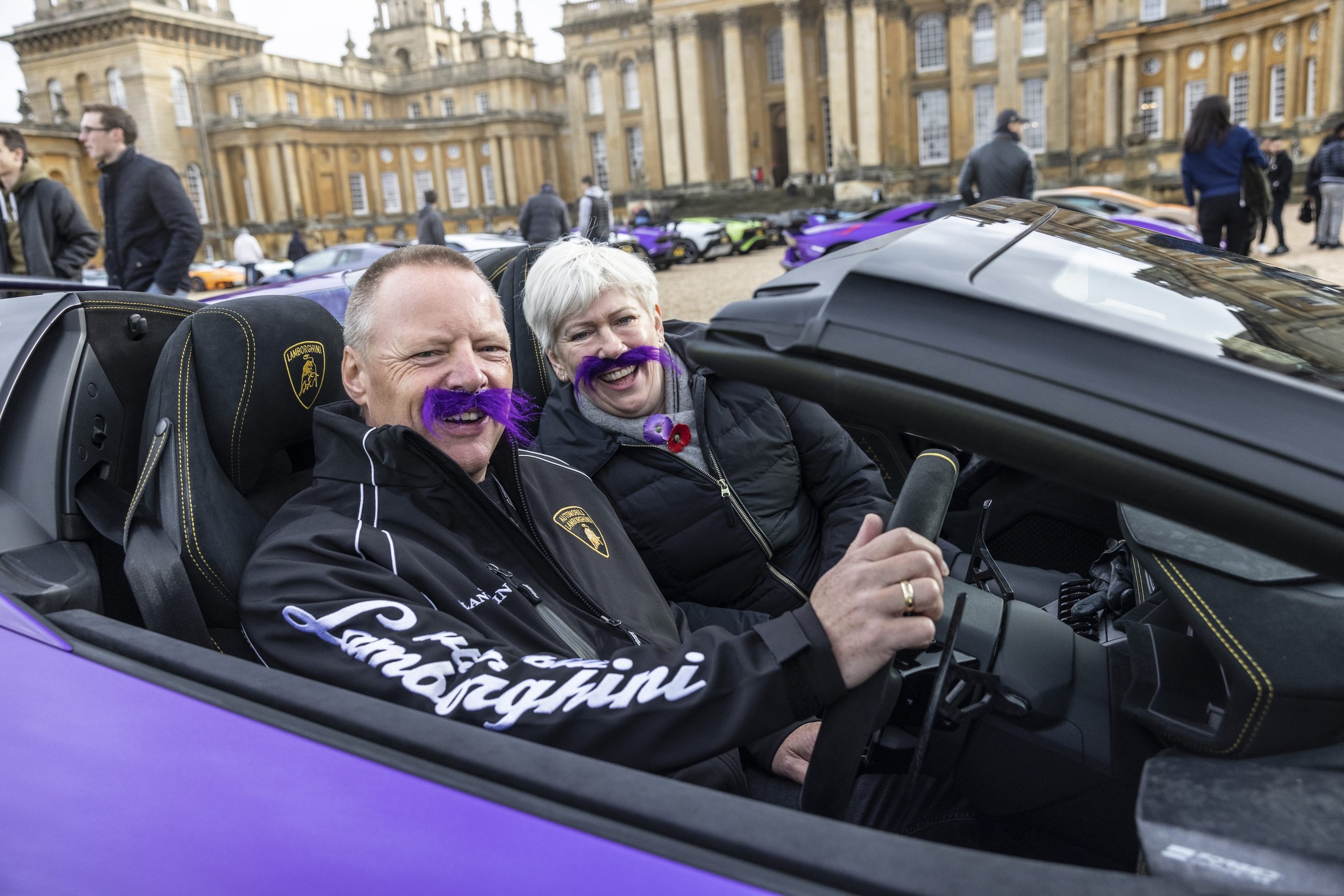 Lamborghini'S Global Movember Bull Run Turned 200 Supercars Into Rolling Billboards For Men'S Health 9 Couple smiling in a purple lamborghini huracán convertible wearing purple movember mustaches at blenheim palace event