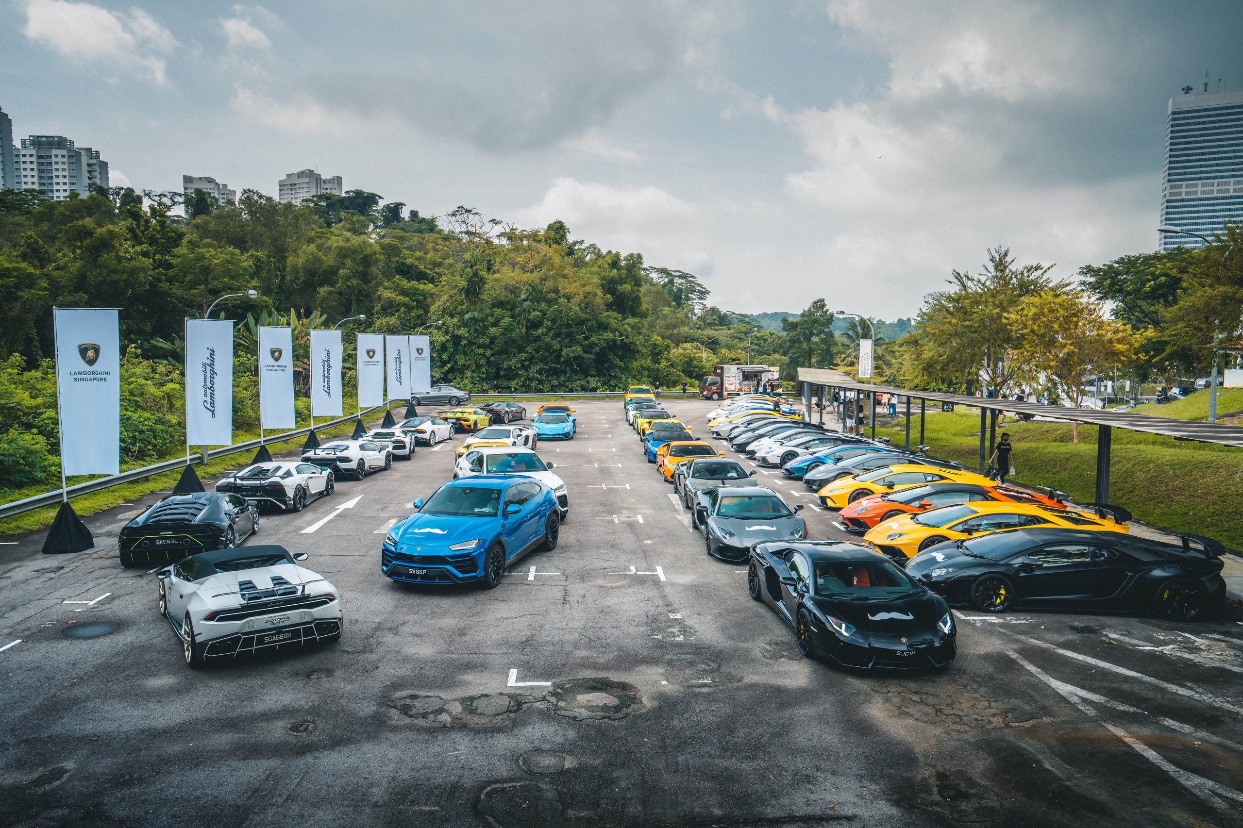 A large gathering of diverse lamborghini vehicles including urus suvs and supercars parked outdoors with event banners