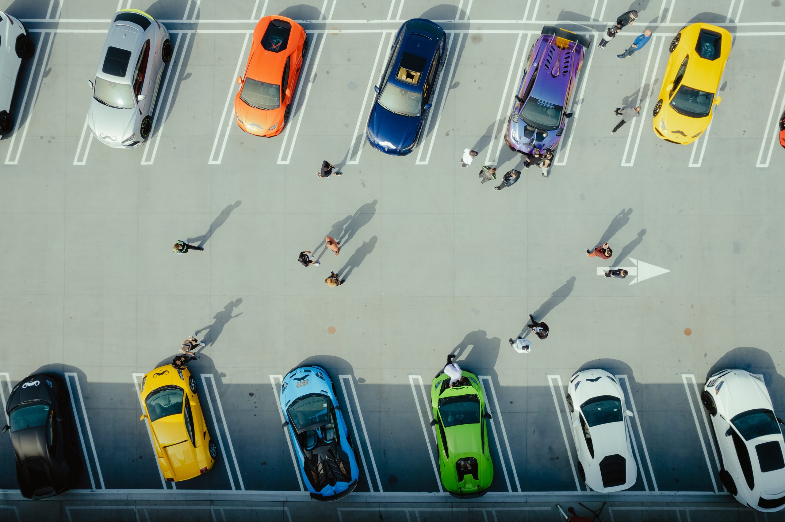 An aerial view of a parking lot filled with various colorful lamborghini vehicles and people walking among them