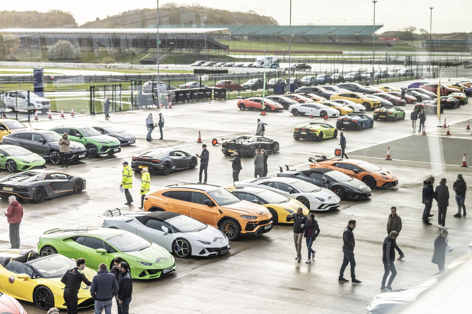 Aerial view of over 200 colorful Lamborghini Huracáns, Aventadors, and Urus SUVs gathered at Silverstone Circuit for the Movember bull run event