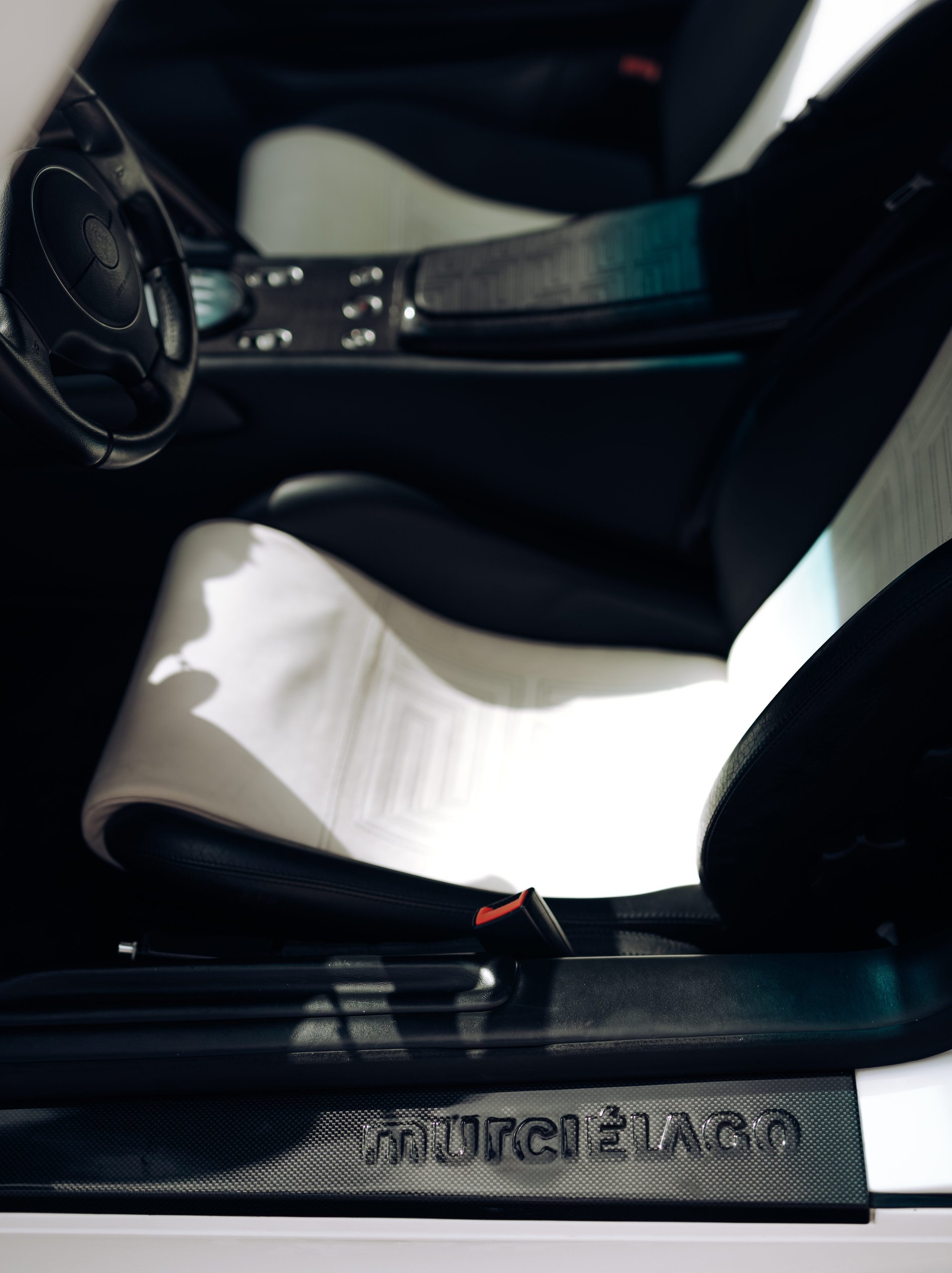 The Murciélago Was Lamborghini'S Last V12 You Could Row Yourself, And That Changes Everything About How We Remember It 7 Close-up of the murciélago interior showing murciélago door sill script and two-tone black and white leather seat