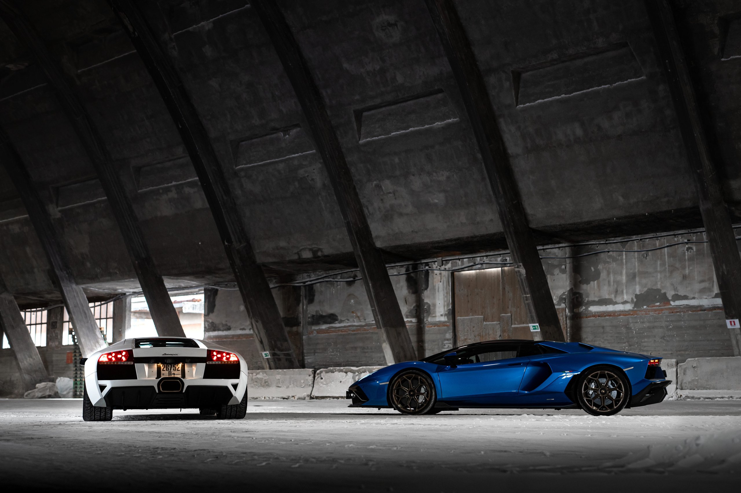 The Murciélago Was Lamborghini'S Last V12 You Could Row Yourself, And That Changes Everything About How We Remember It 11 White lamborghini murciélago and blue lamborghini aventador parked side by side in a large industrial building