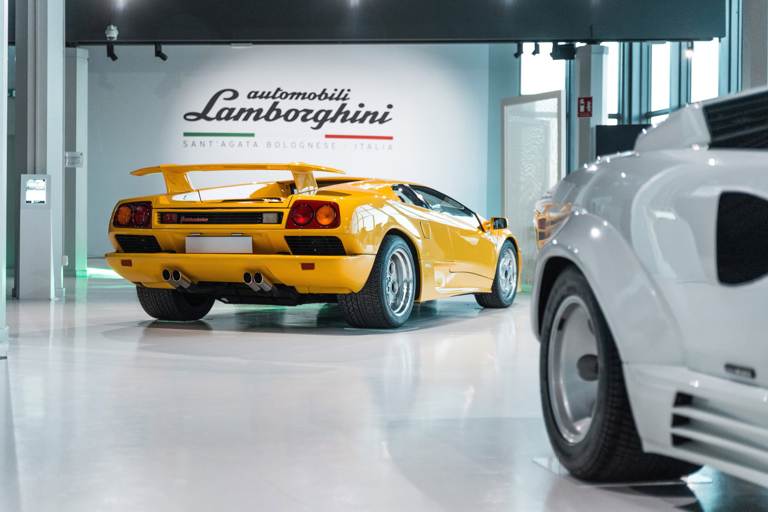 Bright yellow lamborghini diablo displayed from the rear three-quarter angle with a white countach partially visible in the foreground at the lamborghini museum