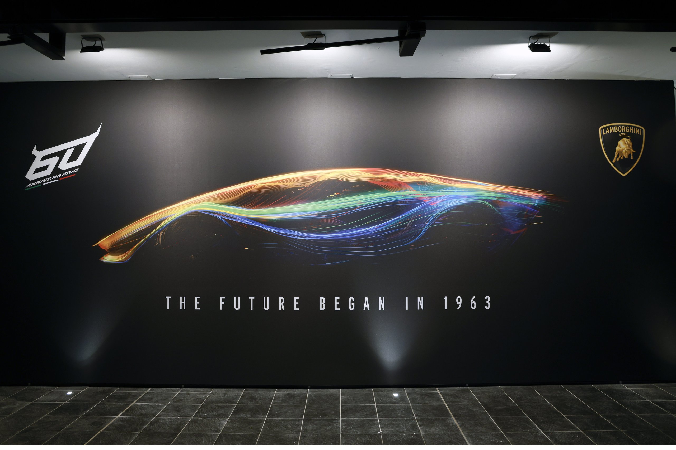 Black wall display featuring the lamborghini 60th anniversary logo, abstract light streak graphic, and 'the future began in 1963' text