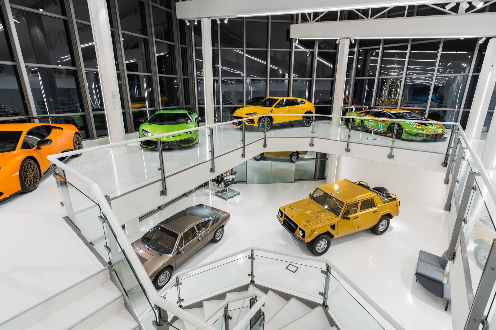 Elevated view of the redesigned Automobili Lamborghini Museum showing multiple levels with a yellow Urus, green Huracán, and classic LM002 on display