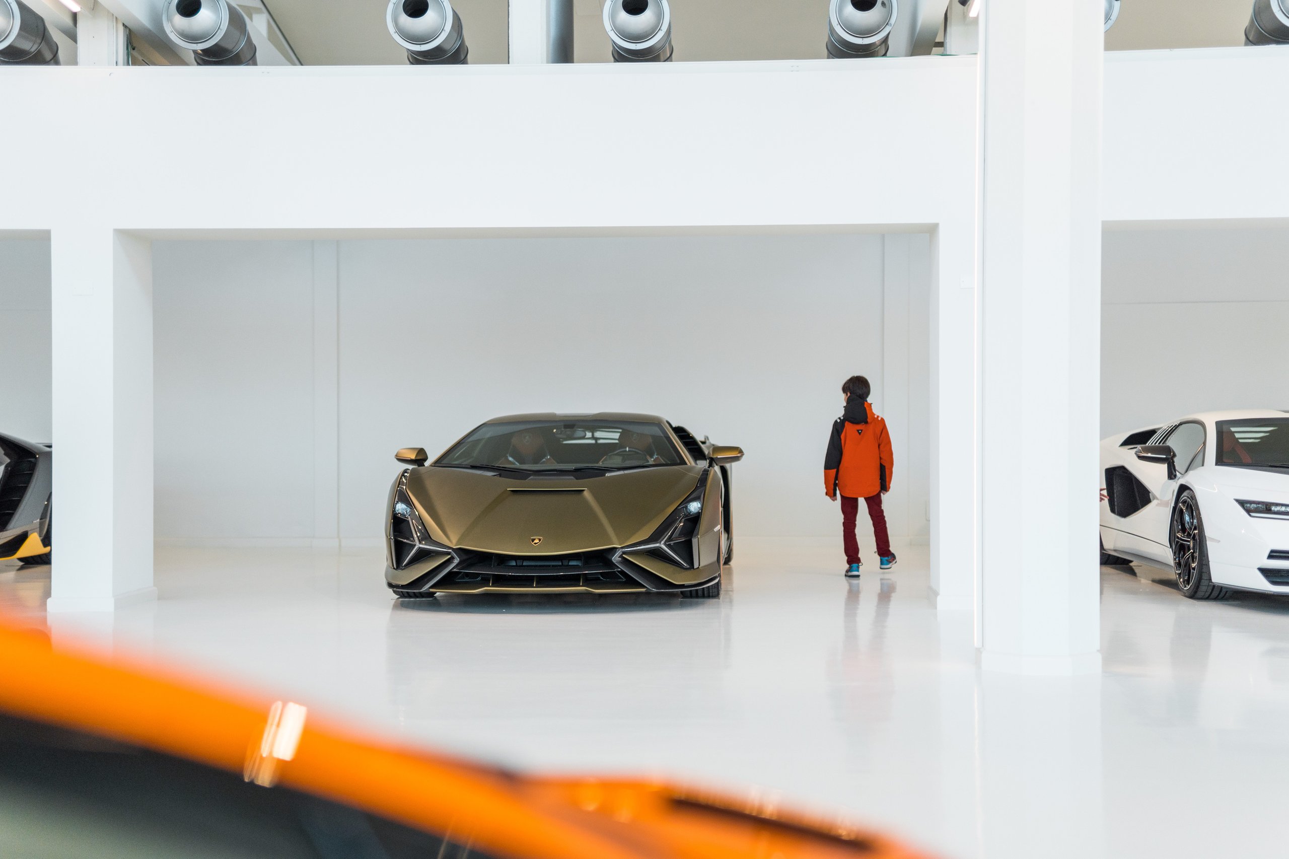 Gold lamborghini sián fkp 37 displayed in a minimalist white showroom with a child standing nearby