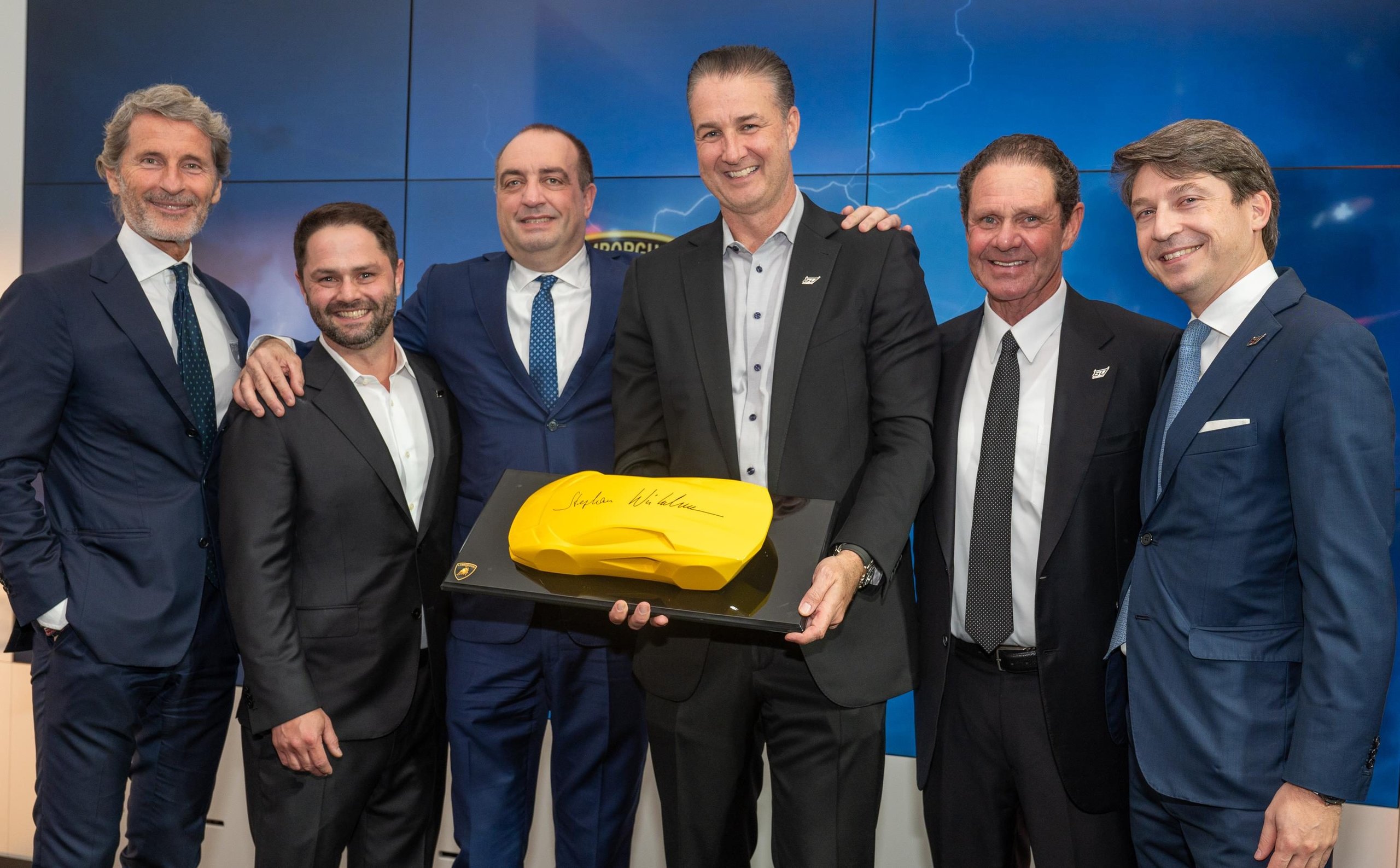 Lamborghini Naples: Why Florida'S Sixth Showroom Tells A Bigger Story About The Brand'S Us Ambitions 3 Lamborghini executives posing with a yellow scale model of the revuelto at the naples showroom grand opening event