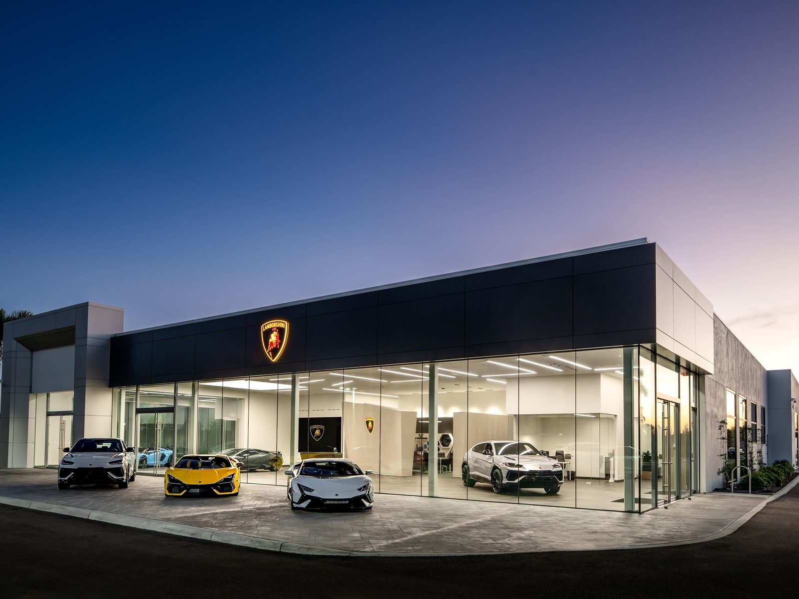 Exterior of the new Lamborghini Naples showroom at dusk with a yellow Revuelto, white Huracan, and grey Urus parked outside