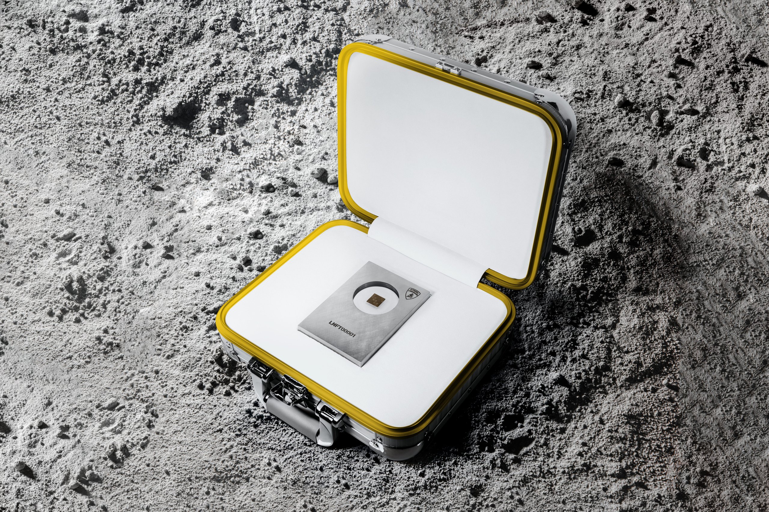 Lamborghini'S Space Key Nft Pairs Iss-Flown Carbon Fiber With Digital Art In A Five-Unit Collector'S Gambit 7 Open silver and yellow protective case containing the lamborghini space key display on a moon-like surface