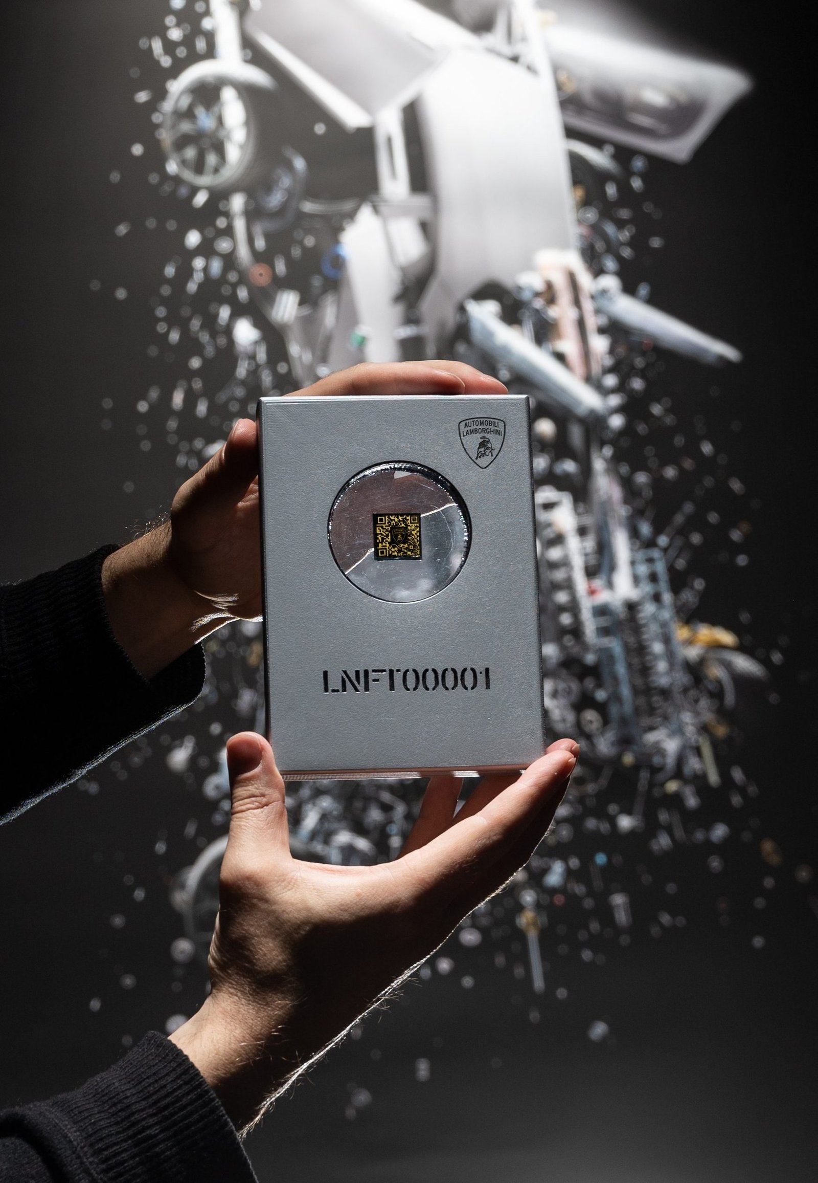 Hands holding a silver Lamborghini-branded Space Key box with a deconstructed Aventador Ultimae artwork visible in the background