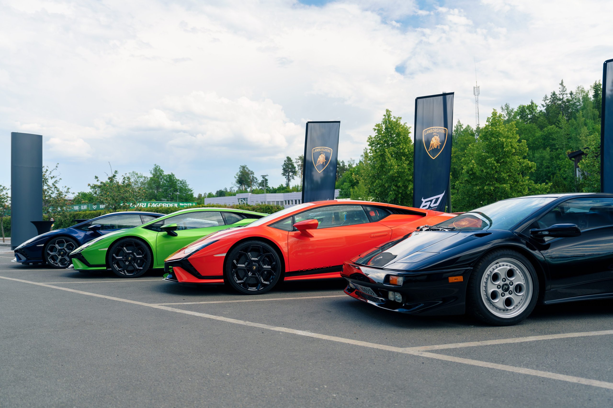 Lamborghini Oslo: Why Norway'S First Showroom Paired A V12 Hybrid Flagship With Frank Sinatra'S Miura 3 Lineup of lamborghini models including a black countach, orange huracán, green huracán, and blue urus at an outdoor event with lamborghini flags