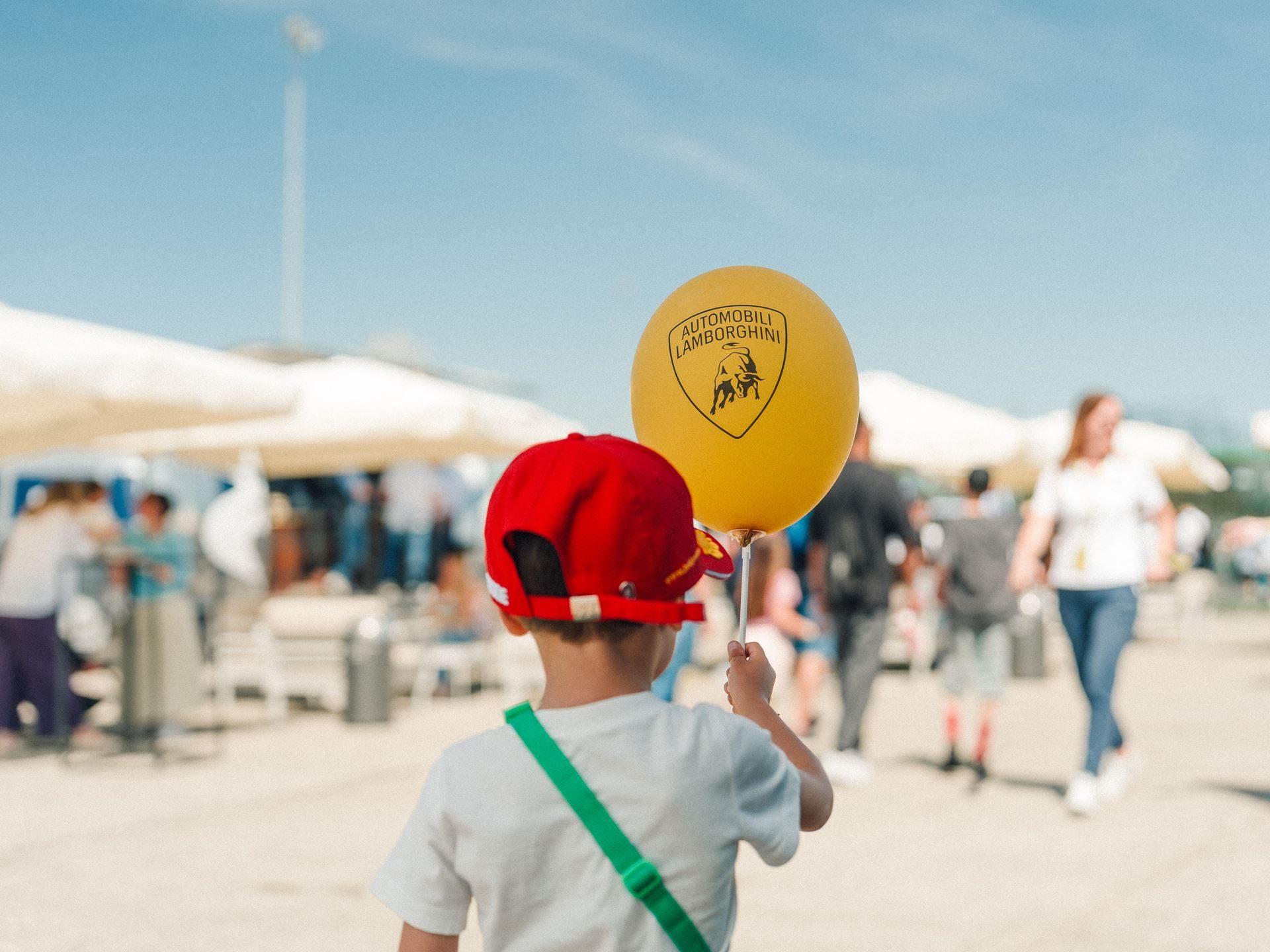 736 Parents In Sant'Agata: Inside Lamborghini'S Workplace Support Package For Employee Families 5 A young child seen from behind holding a yellow balloon with the automobili lamborghini logo at an outdoor event