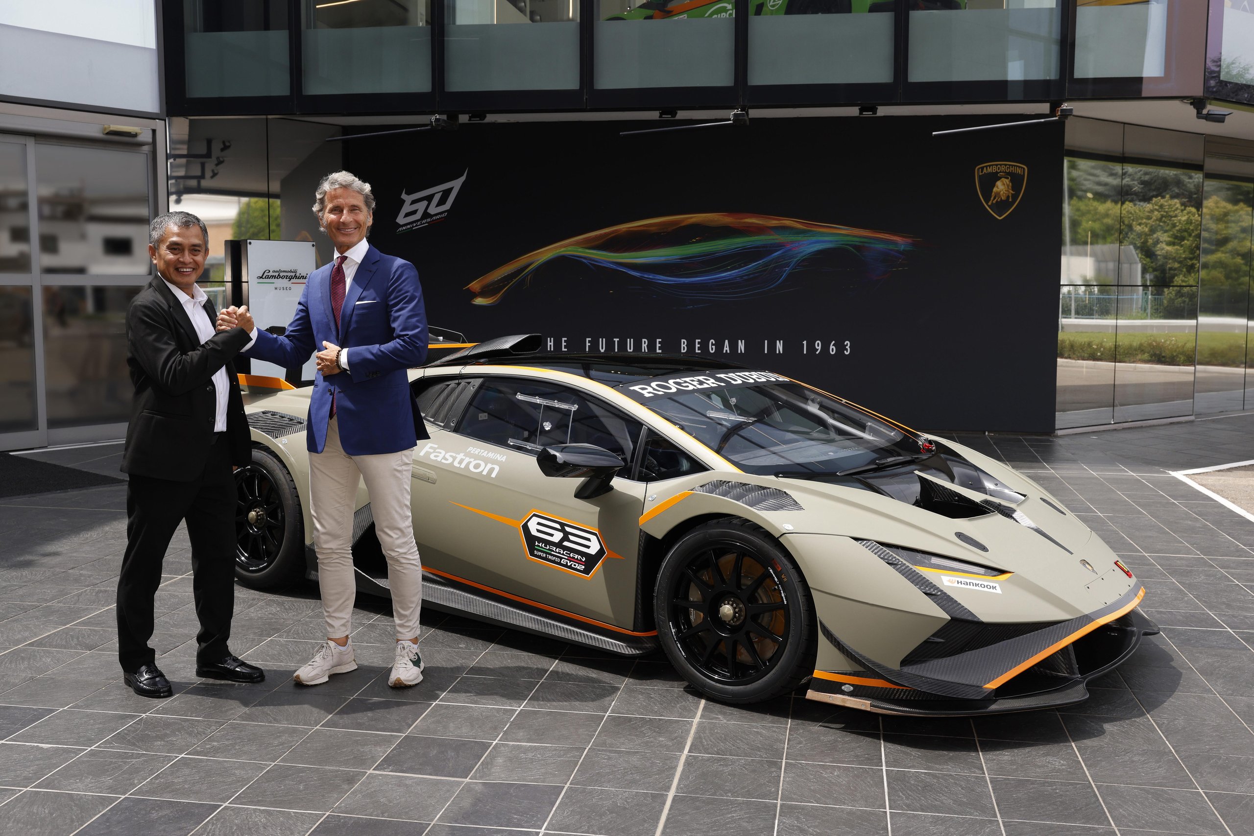 Lamborghini Renews Pertamina Lubricant Partnership Through 2025, Covering Super Trofeo, Gt3, And Sc63 Lmdh 5 Two men shaking hands next to a lamborghini huracan super trofeo evo2 at outdoor event with 60th anniversary backdrop