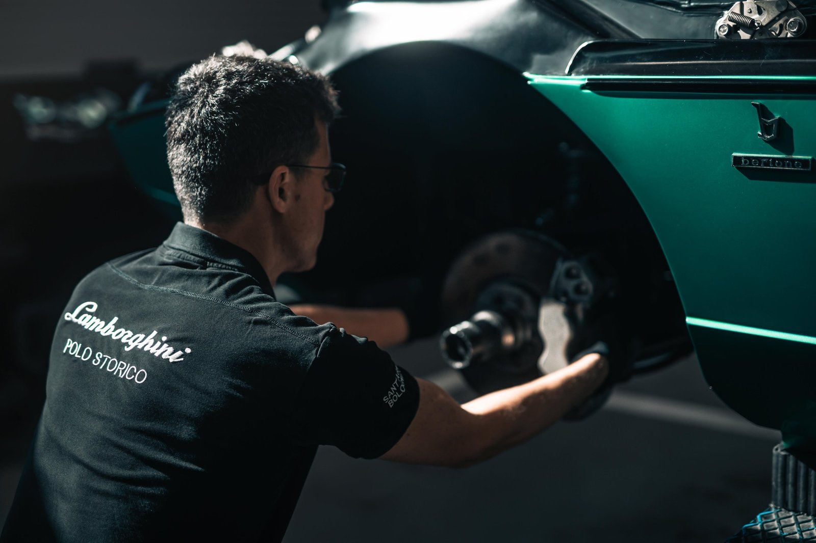 Lamborghini Polo Storico technician working on the brake assembly of a classic green Miura in the Sant'Agata Bolognese workshop
