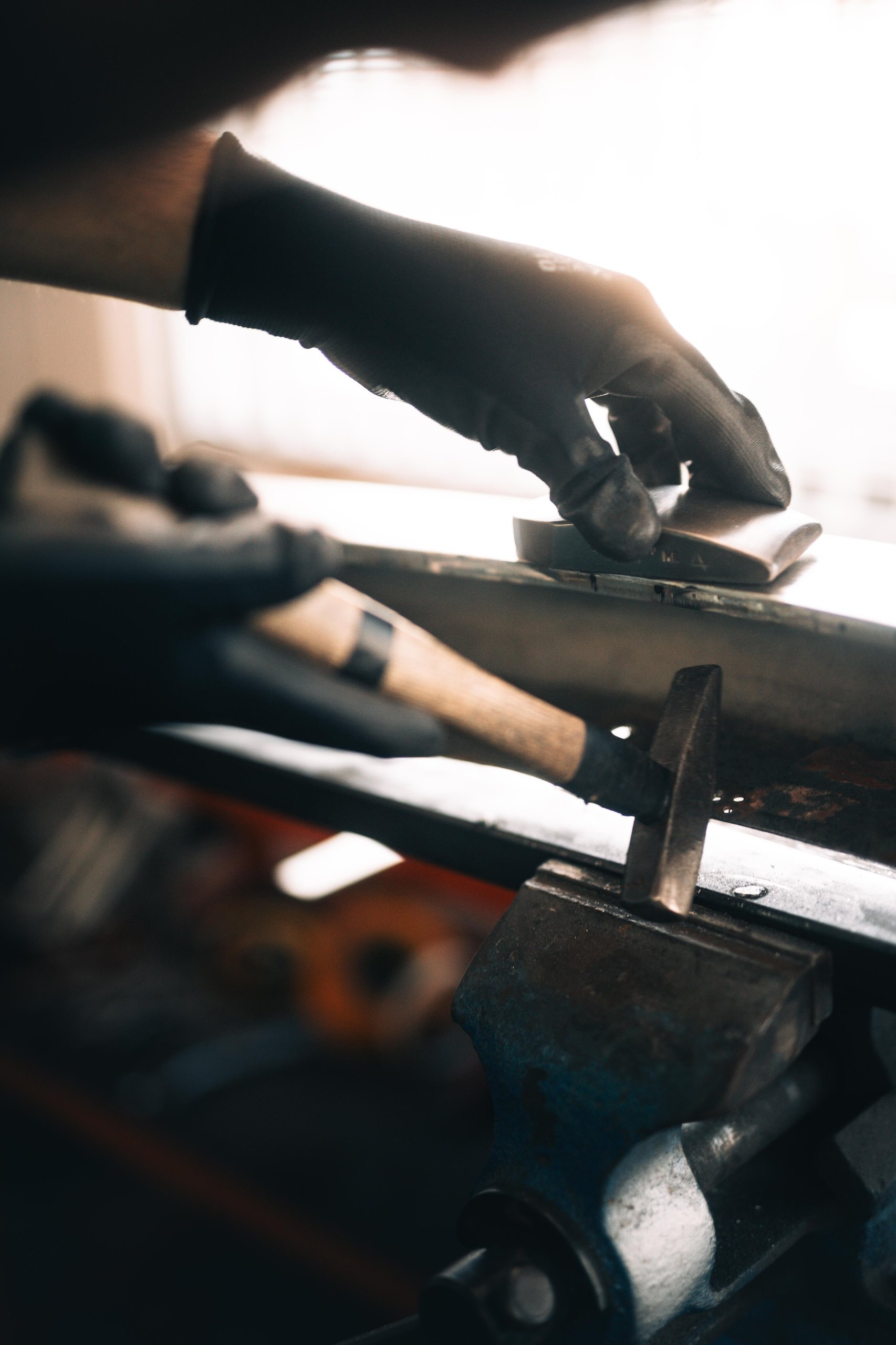 Polo Storico At Ten: Why Lamborghini Let Collectors Get Their Hands Dirty In Sant'Agata 7 Gloved hand using a hammer to shape a metal component held in a vise during classic lamborghini restoration