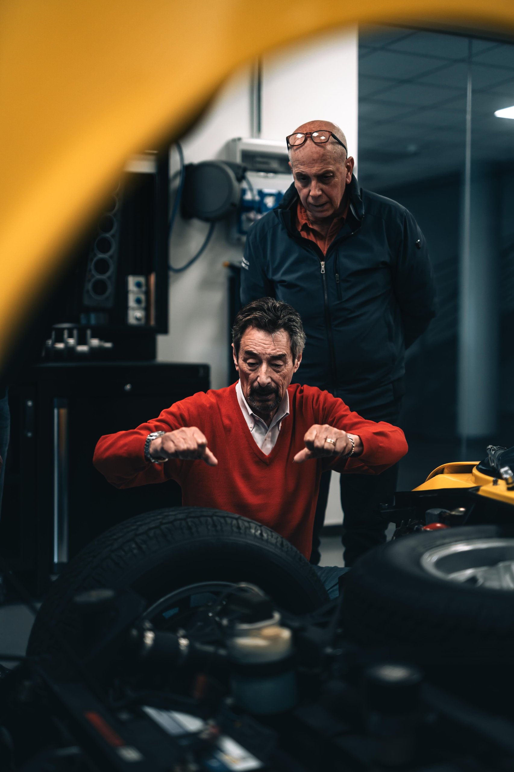 Two men inspecting the engine bay of a classic yellow Lamborghini Miura in the Polo Storico workshop