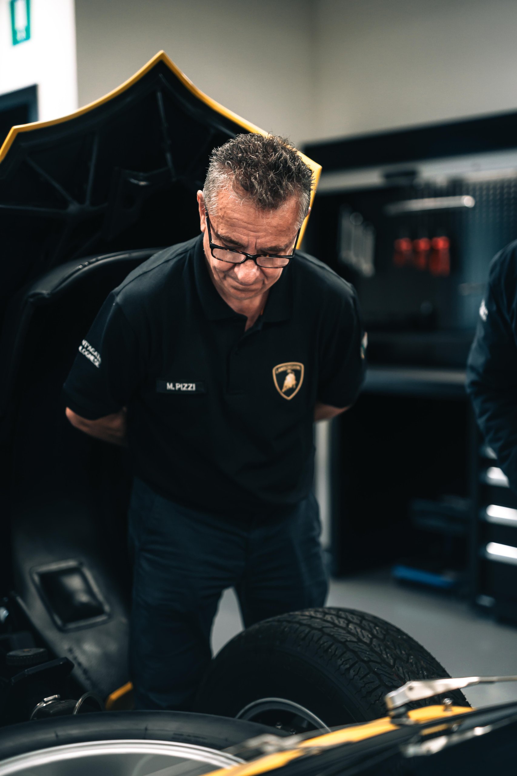 Massimo Pizzi inspecting the engine bay of a classic yellow Lamborghini Countach LP400 in the Polo Storico workshop