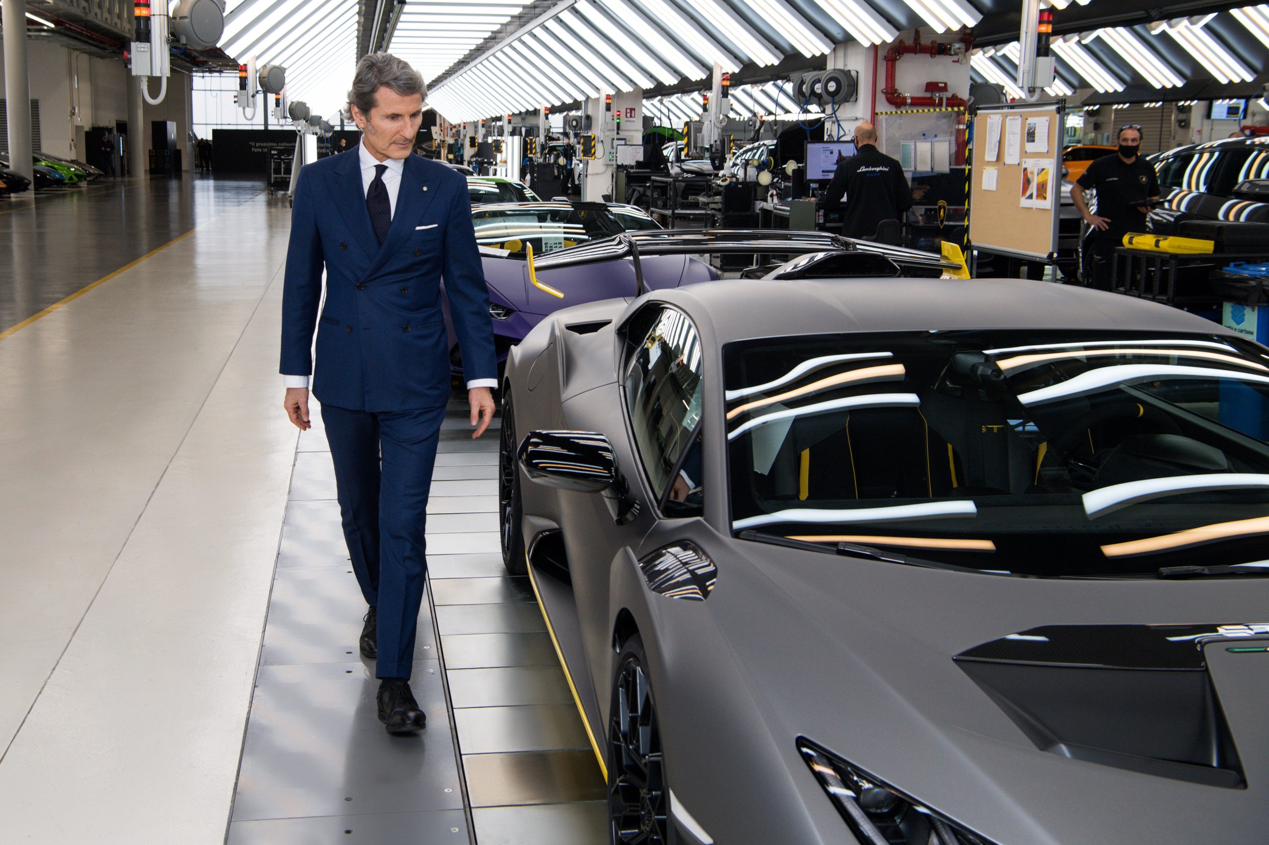 Lamborghini'S Q1 2022 Proves The Power Of Saying No: €178 Million In Profit By Selling Less Than The Market Wants 9 A man in a suit walking through the lamborghini factory floor past huracán models in various stages of assembly
