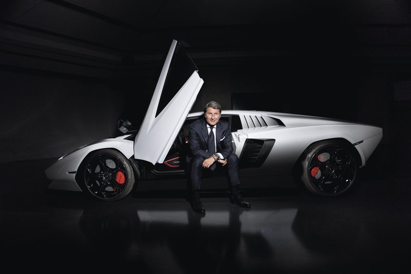Stephan Winkelmann, CEO of Lamborghini, seated on the sill of a white Lamborghini Countach LPI 800-4 with its scissor door open