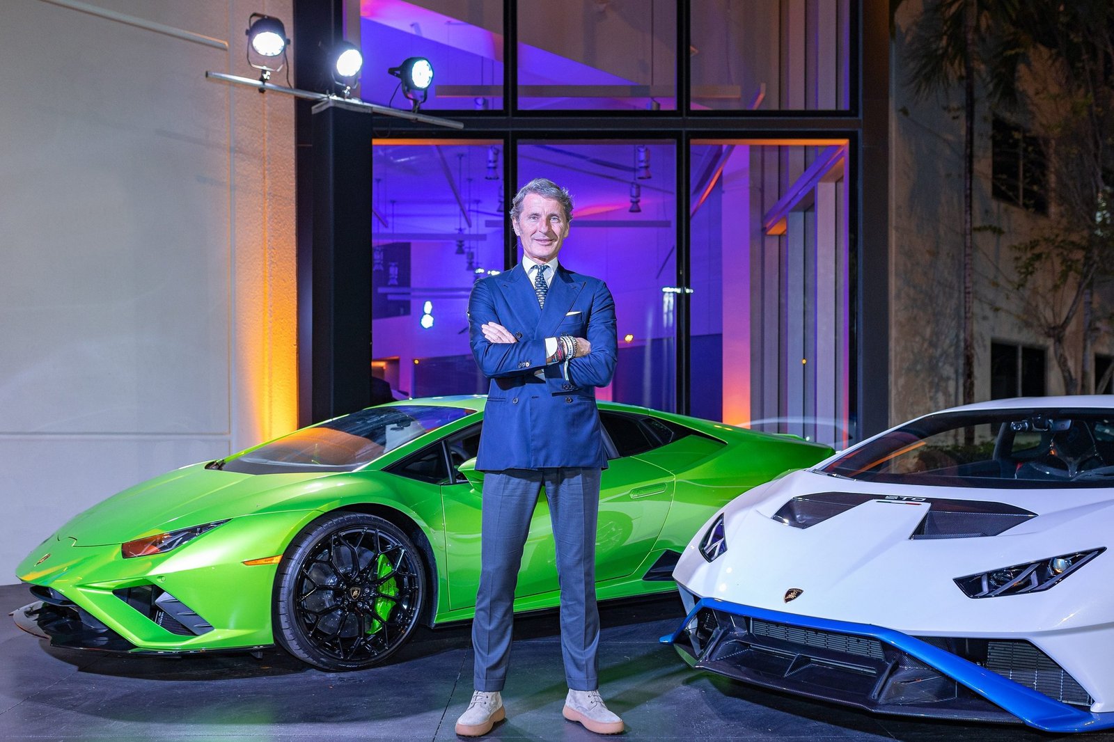 Stephan Winkelmann, CEO of Automobili Lamborghini, standing between a green Huracán Tecnica and a white Huracán STO at a U.S. showroom event