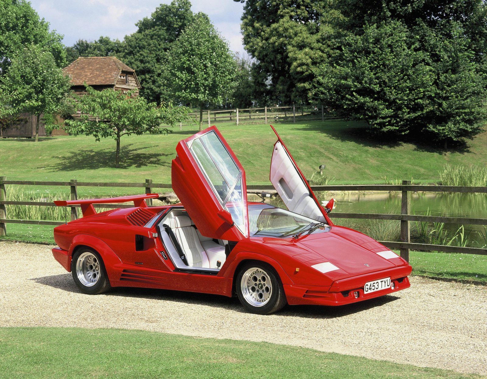 Red Lamborghini Countach 25th Anniversary with scissor doors open on a green rural driveway