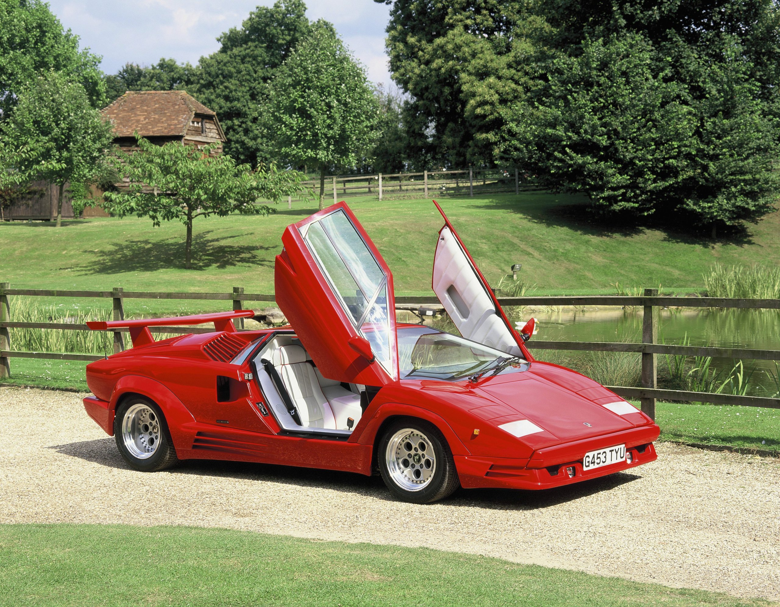 Red lamborghini countach 25th anniversary with scissor doors open on a green rural driveway