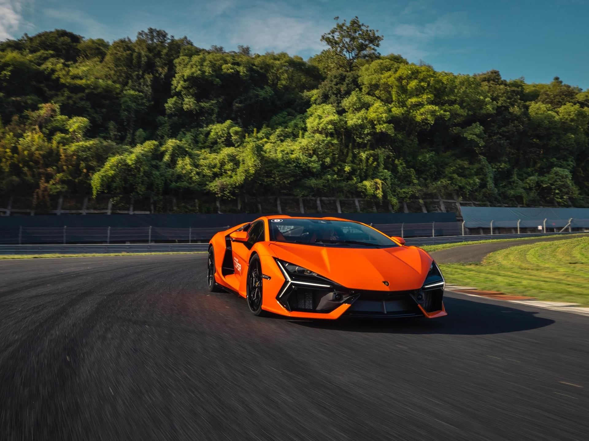 Lamborghini Brought The Revuelto To A Chinese Racetrack To Prove Its V12 Hybrid Belongs There 5 Orange lamborghini revuelto mid-turn on the zhejiang circuit with blurred trees and blue sky in the background