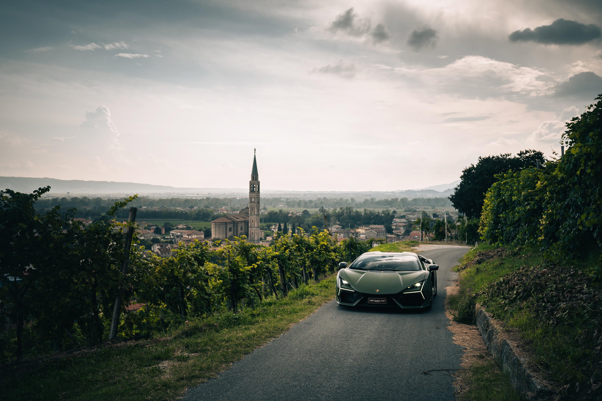 Lamborghini Sent The Revuelto Across Italy To Prove A 1,001 Hp Hybrid Can Still Be A Proper V12 Flagship 7 Dark green lamborghini revuelto parked overlooking a picturesque italian village with vineyards and a church spire