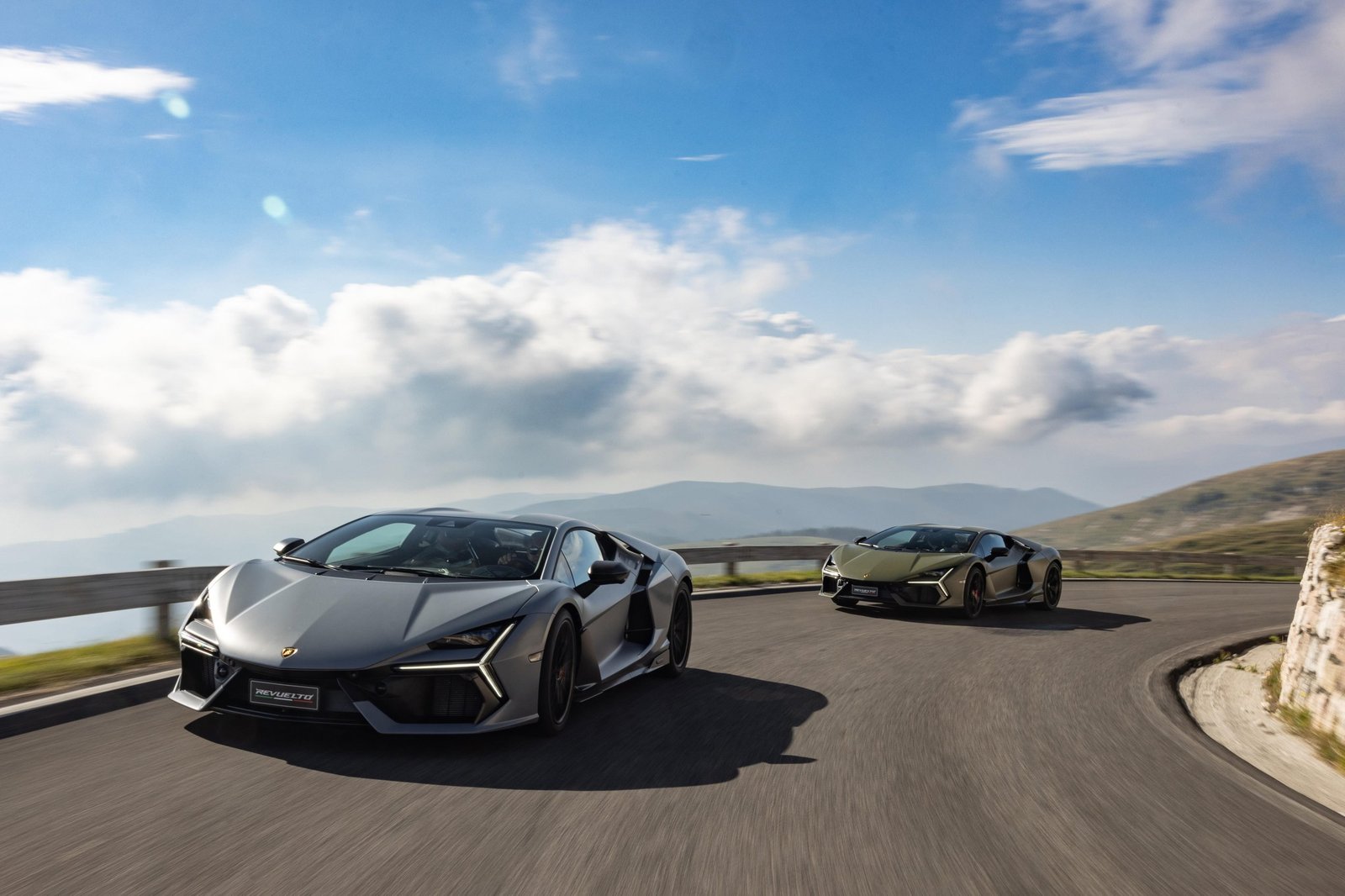 Two Lamborghini Revueltos in grey and olive green driving on a winding Italian mountain road