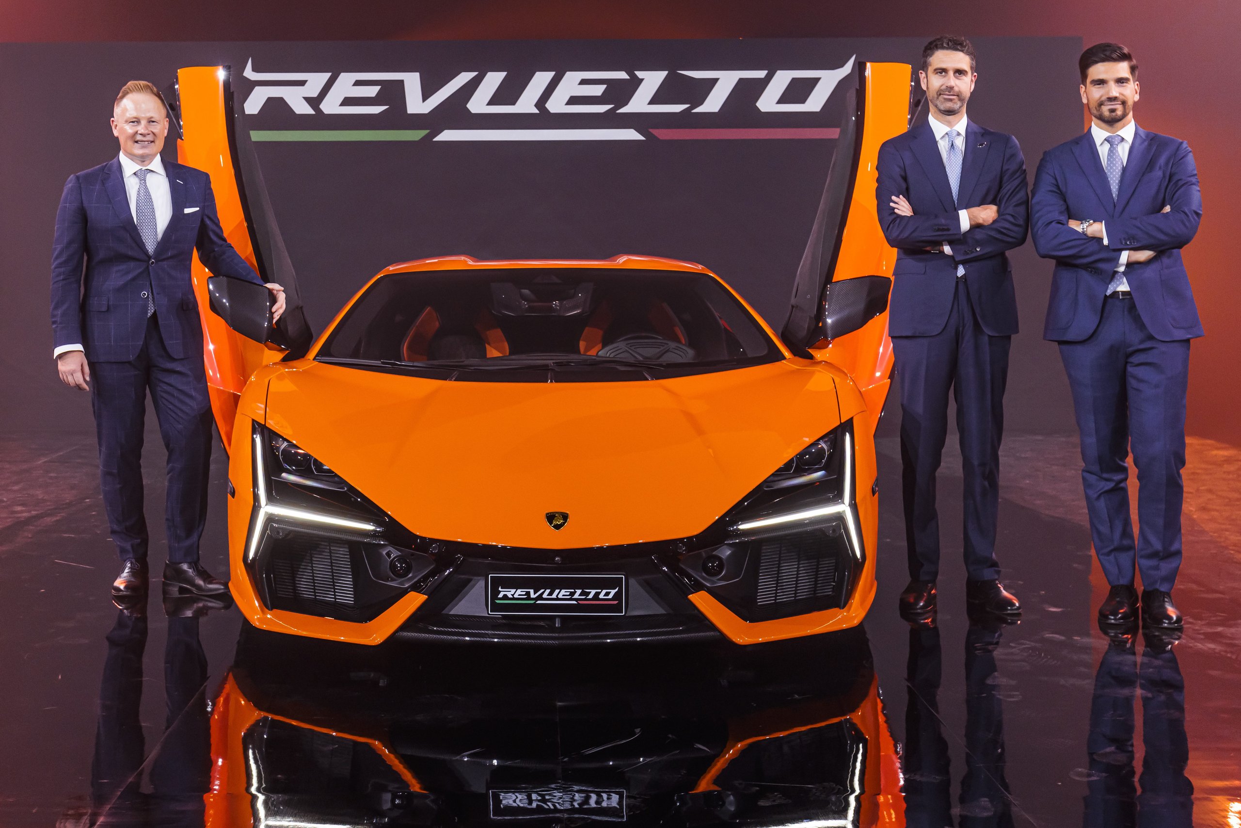 Lamborghini Brought Six Decades Of V12 History To Tokyo'S Ariake Arena, Then Unveiled What Comes Next 5 Three lamborghini executives standing with the orange revuelto with scissor doors open at the japan premiere