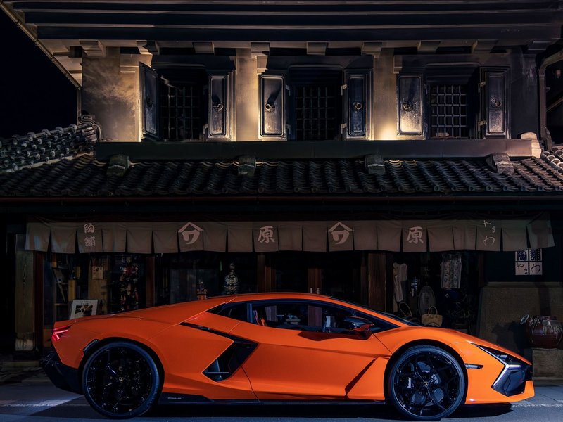 Orange Lamborghini Revuelto parked at night in front of a traditional Japanese building with illuminated windows
