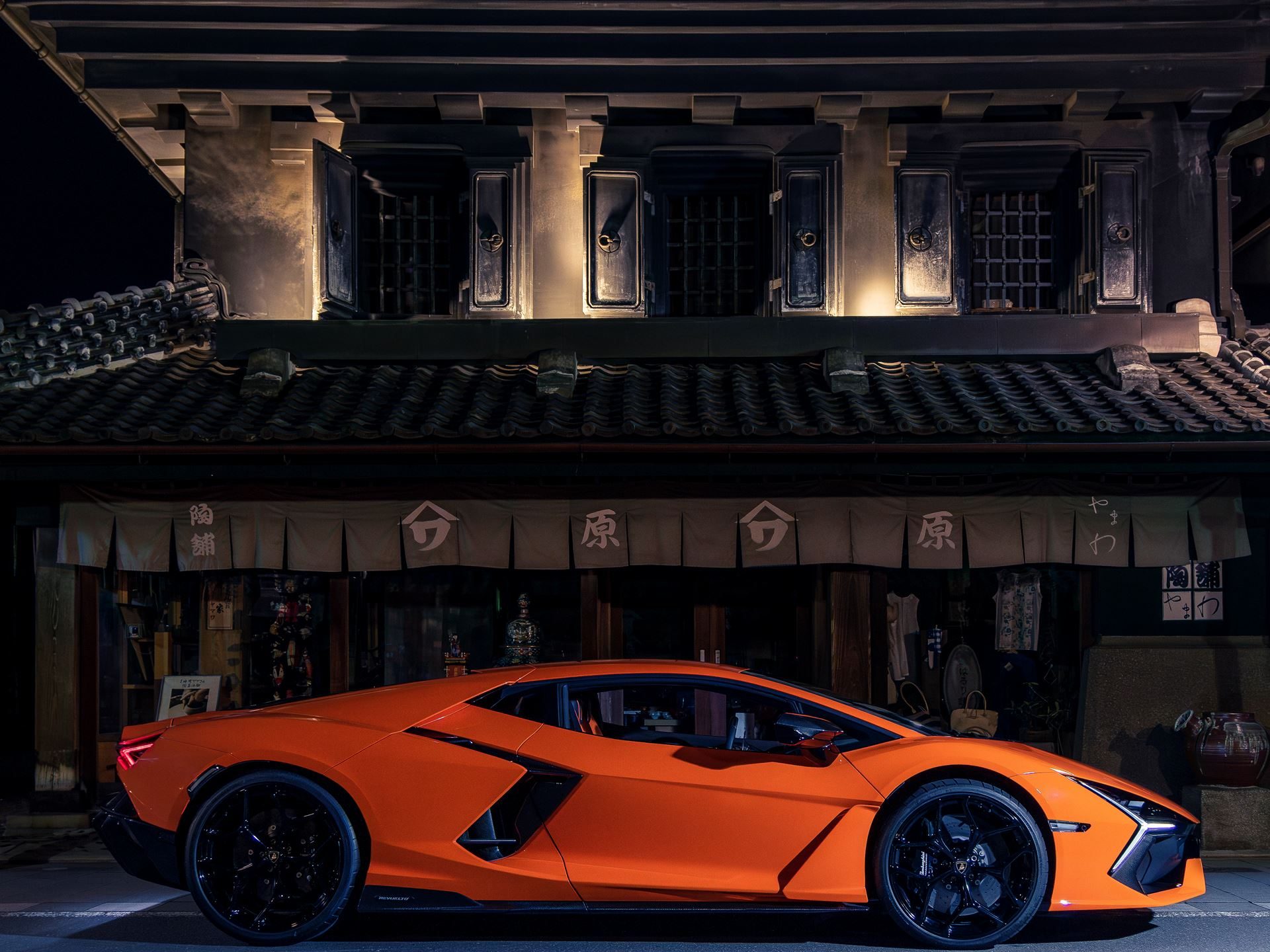 Orange lamborghini revuelto parked at night in front of a traditional japanese building with illuminated windows