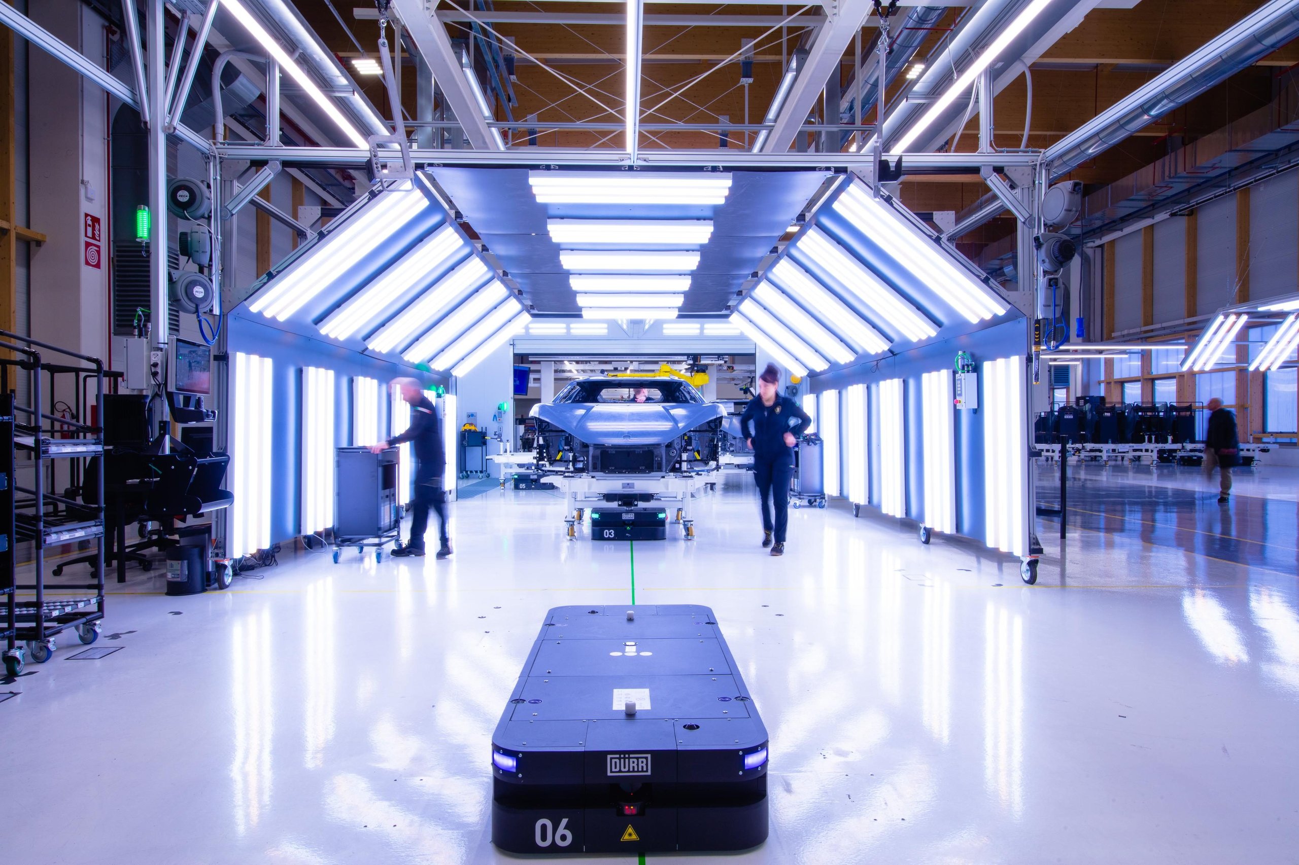 500 Humans, A Fleet Of Cobots, And One Carbon Fiber Tub: How Lamborghini Actually Builds The Revuelto 7 An automated guided vehicle approaches a revuelto chassis under inspection lights on the factory floor
