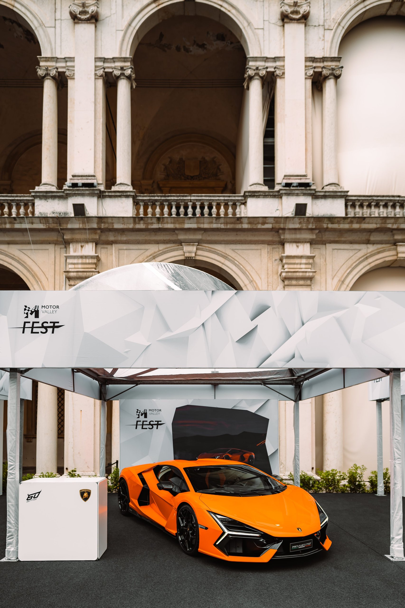 Motor Valley Fest 2023 Was Lamborghini'S First Public Statement That The Revuelto Era Had Arrived 3 Orange lamborghini revuelto displayed under a white tent at motor valley fest 2023 with classical arched architecture visible in the background
