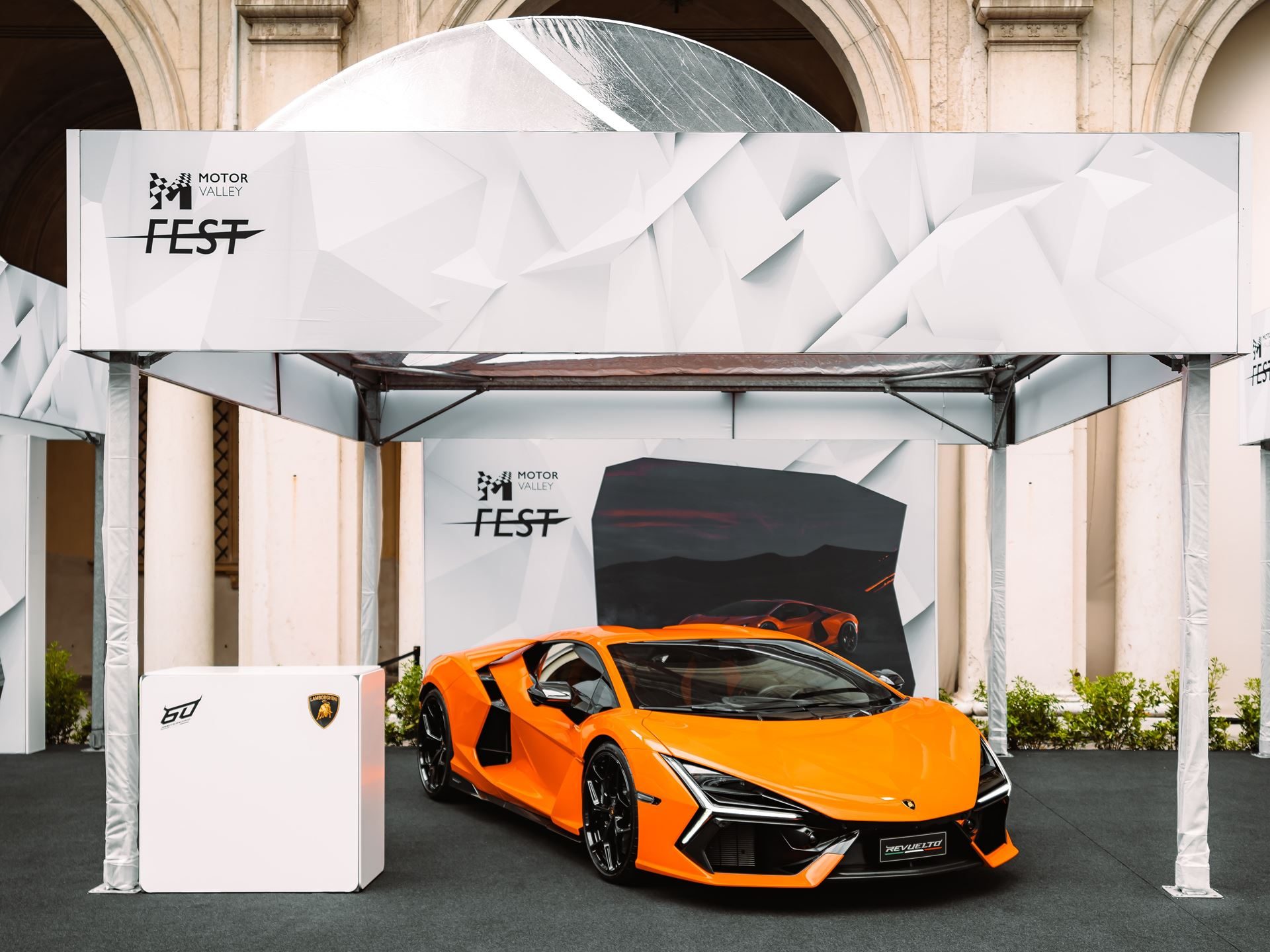 Motor Valley Fest 2023 Was Lamborghini'S First Public Statement That The Revuelto Era Had Arrived 9 Orange lamborghini revuelto displayed under a white tent at motor valley fest 2023 with geometric patterns and event logo in the background