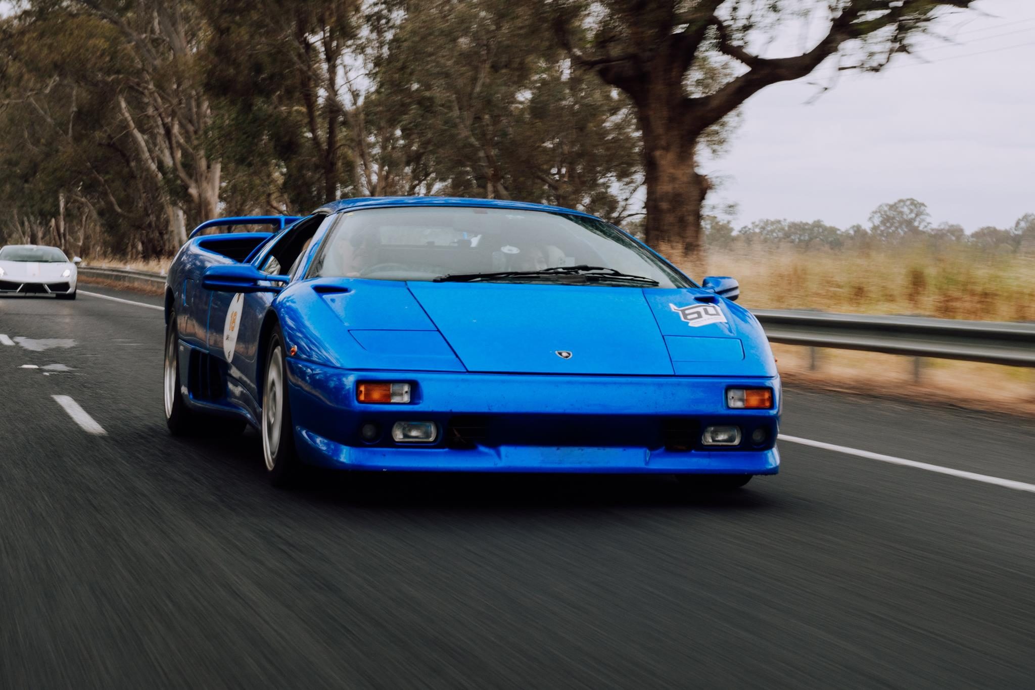 Classic blue lamborghini diablo driving on an open road surrounded by blurred trees