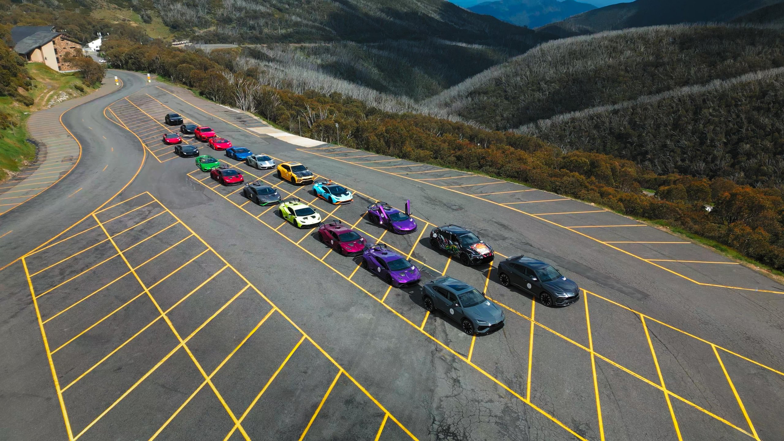 How Lamborghini Turned Melbourne Into A Rolling Museum For The Revuelto'S Oceania Debut 15 Aerial view of dozens of colorful lamborghini vehicles gathered in a parking area with mountains in the background during the esperienza giro oceania