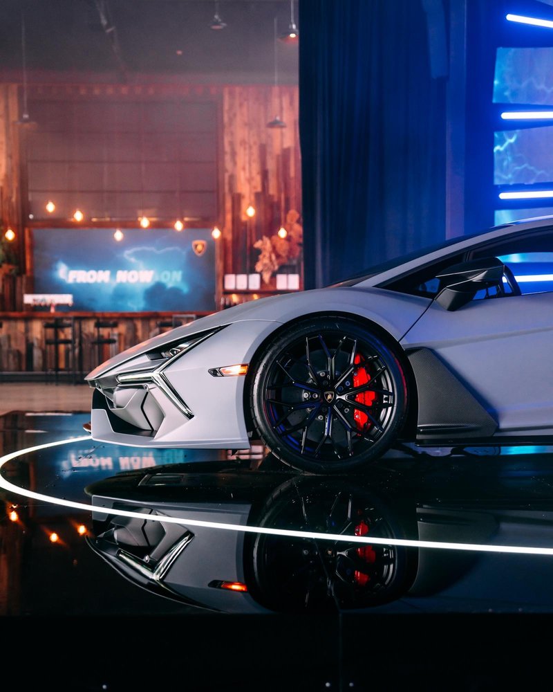 Matte grey Lamborghini Revuelto front quarter view showing aggressive styling, red brake calipers, and neon-lit background