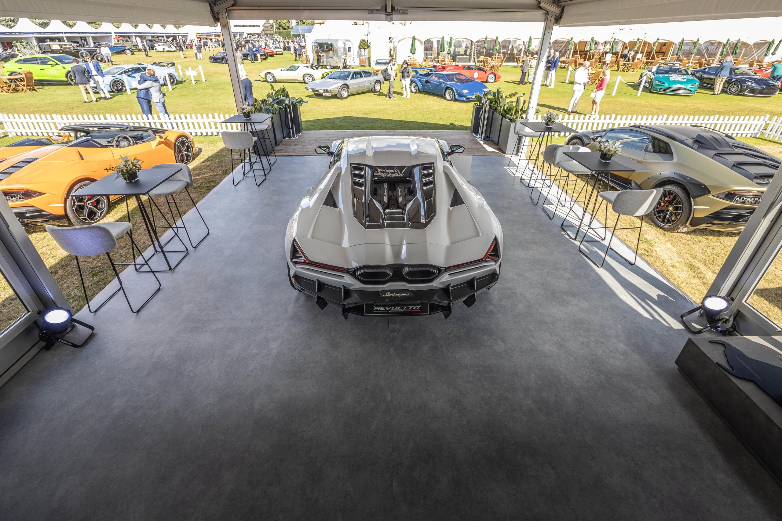 Sixty V12 Lamborghinis At Blenheim Palace: How Salon Privé Became The Revuelto'S Most Strategic Uk Stage 7 Overhead view of a white lamborghini revuelto on display with an orange huracán and matte gold huracán sterrato visible nearby