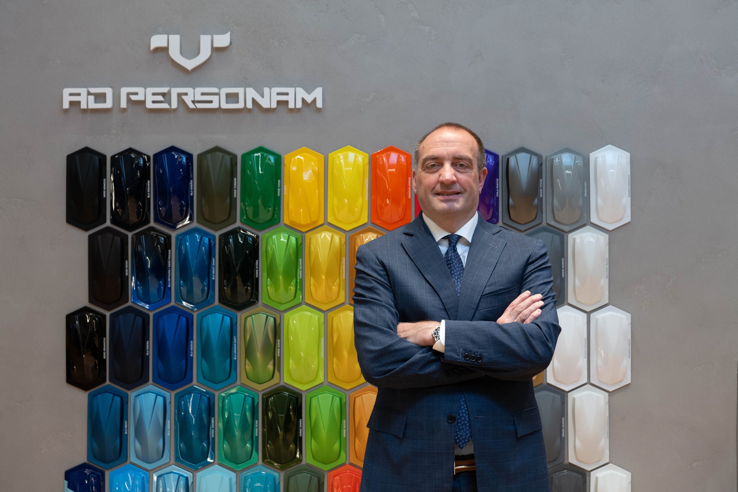 A lamborghini executive standing in front of a wall displaying numerous ad personam paint samples in various colors and finishes