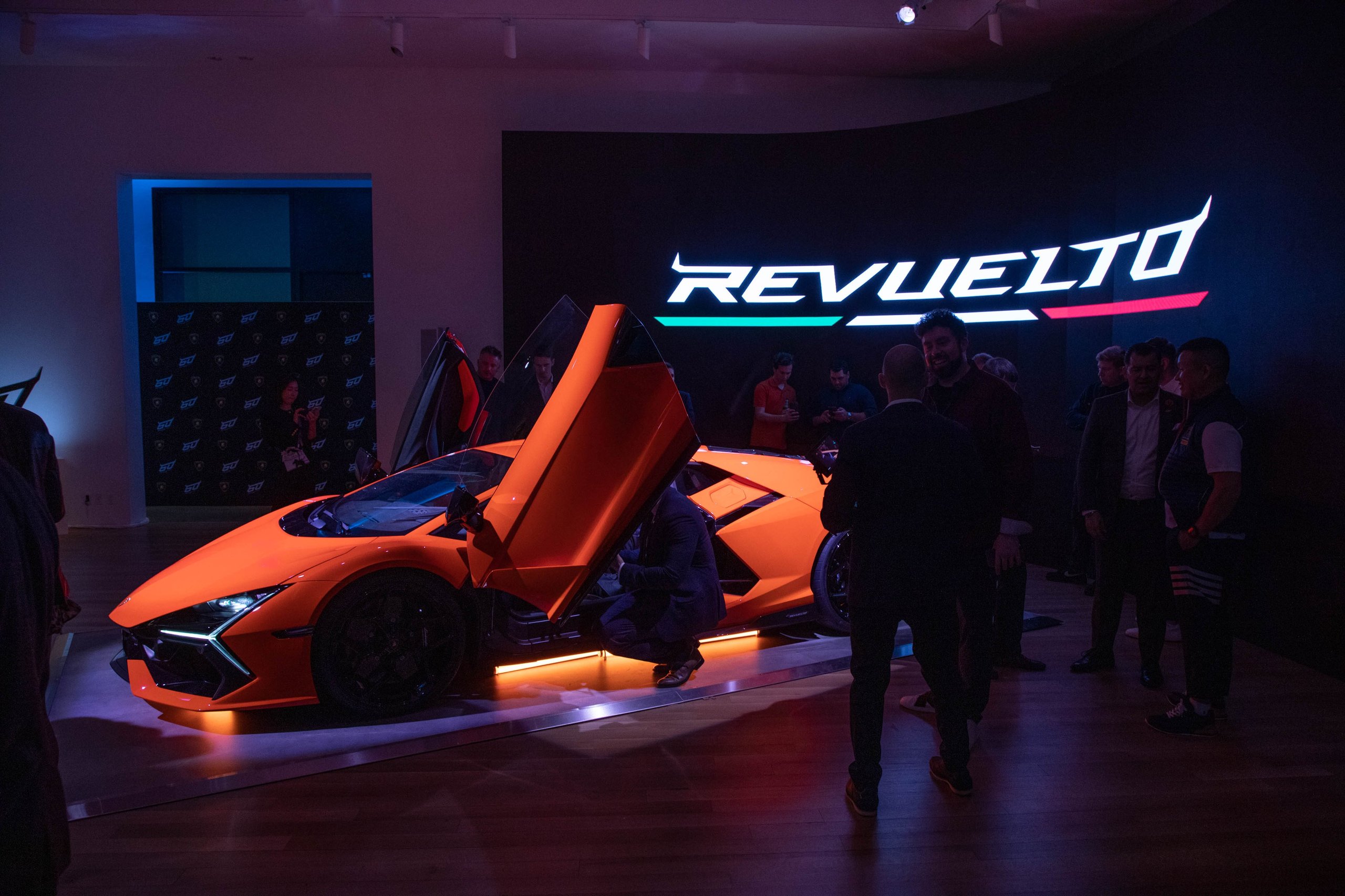 Wide shot of the orange lamborghini revuelto with scissor doors open, surrounded by attendees at the evening premiere event