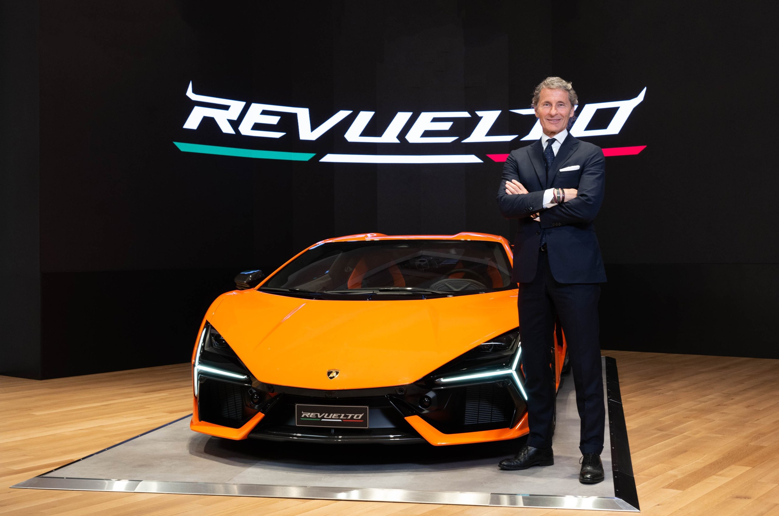 Stephan winkelmann, ceo of automobili lamborghini, standing next to the orange revuelto at its us premiere
