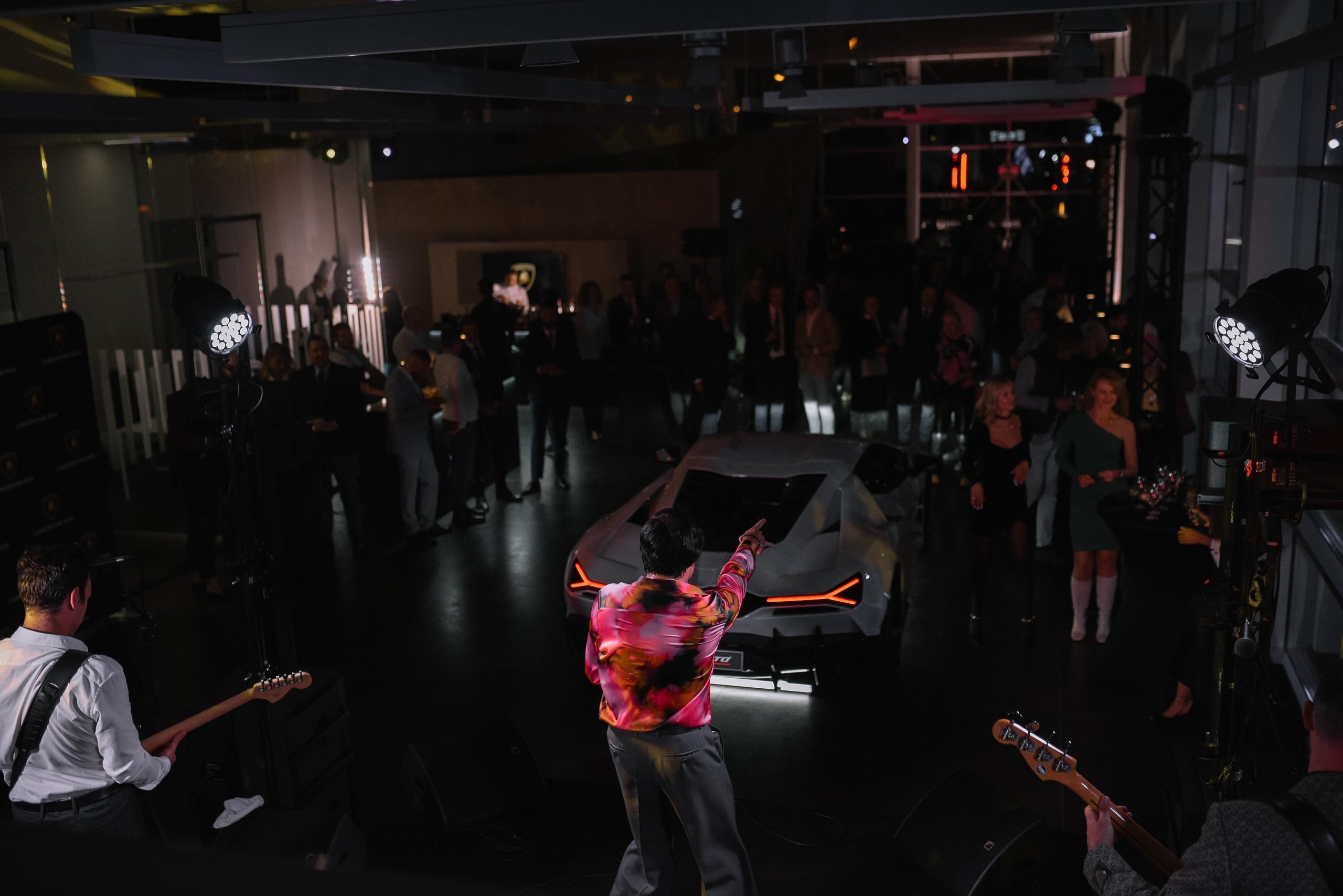 Lamborghini Riga: Why The Brand'S First Latvian Showroom Doubles As A Hybrid-Era Statement 3 A live band performs in front of a white lamborghini revuelto at the riga showroom grand opening event with guests mingling in the background
