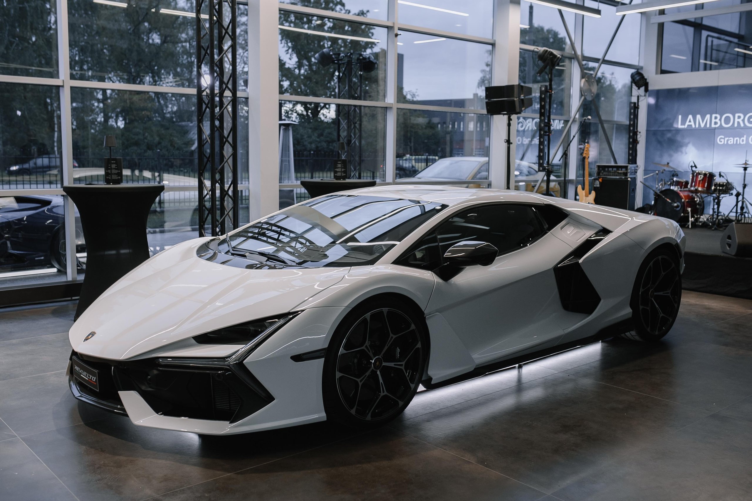 Lamborghini Riga: Why The Brand'S First Latvian Showroom Doubles As A Hybrid-Era Statement 7 A white lamborghini revuelto displayed in the modern riga showroom with stage lighting and large windows