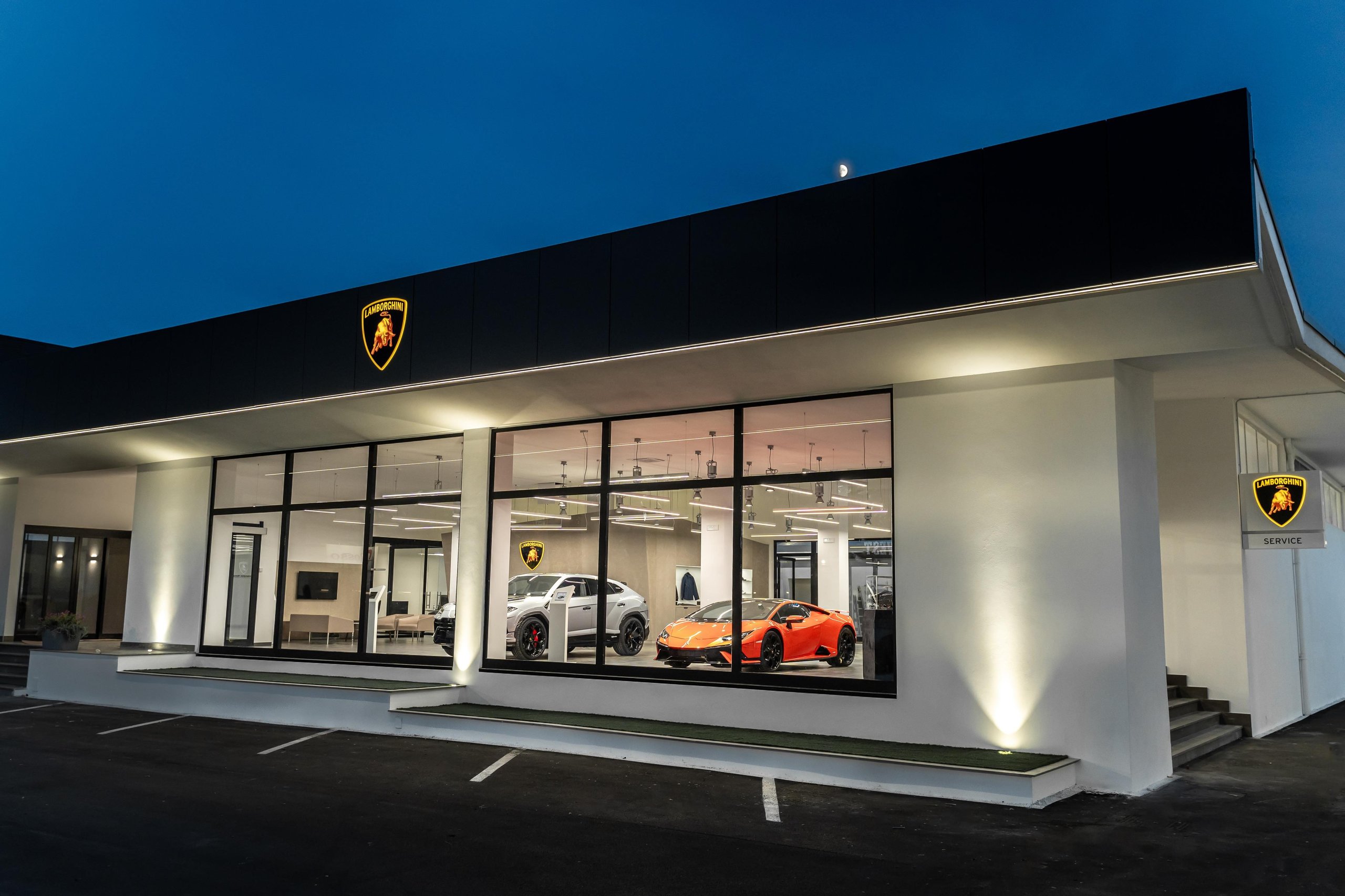 Lamborghini'S New Rome Flagship Pairs A Miura With The Revuelto To Sell Its Electrified Future 13 Exterior of the new lamborghini rome dealership at dusk with illuminated logo and vehicles visible through the glass facade