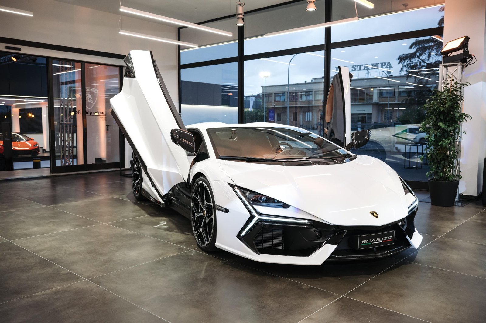 White Lamborghini Revuelto with scissor doors open displayed in the new Lamborghini Rome dealership showroom