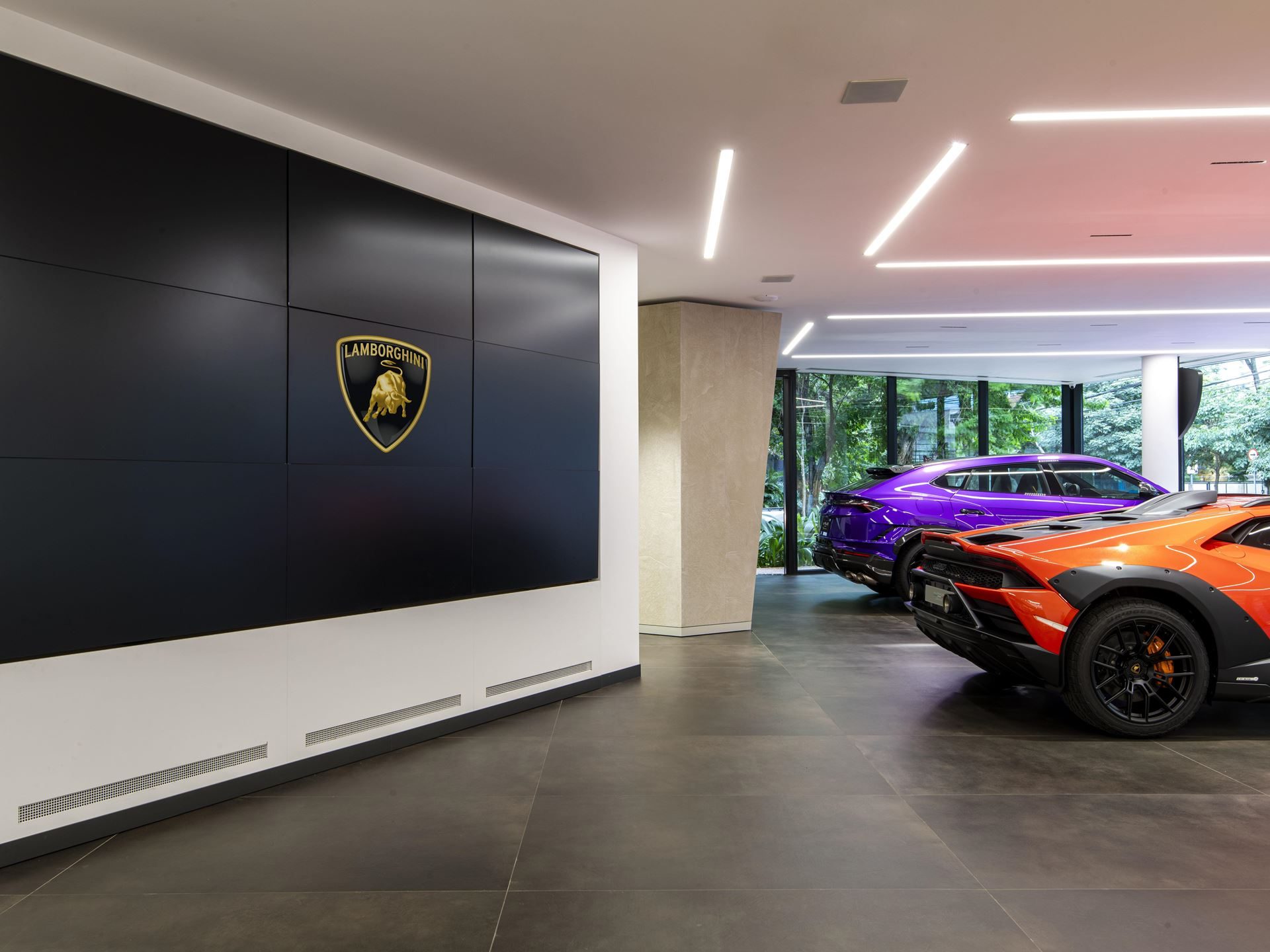 Lamborghini Opens Its First São Paulo Showroom With The Sterrato'S South American Debut, Laying The Ground For A Hybrid Future 9 Interior of the lamborghini são paulo showroom with the lamborghini shield logo on a black wall, purple urus and orange huracán sterrato on display